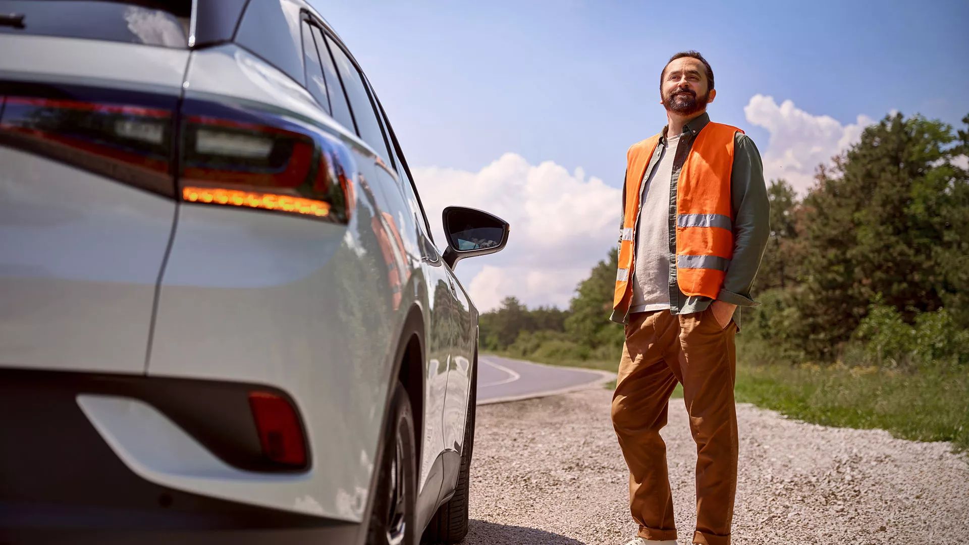 Muž v reflexnej veste stojí vedľa svojho VW ID. na okraji cesty.