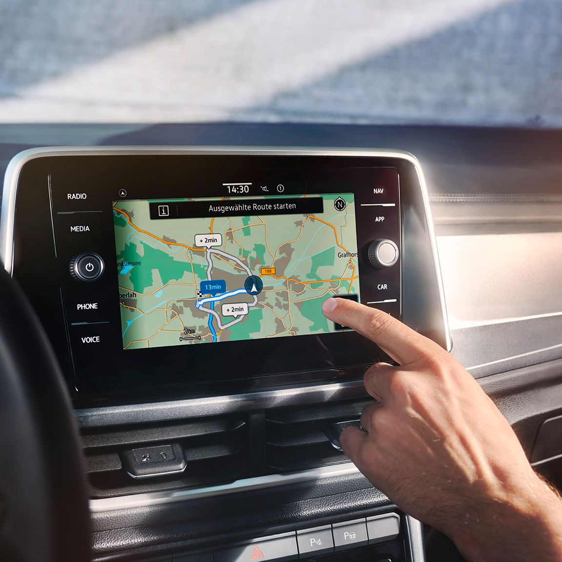 Interiér VW T-Roc, detailný pohľad na displej systému infotainment Discover Media s navigačnou mapou a ruka človeka, ktorý ovláda navigáciu.