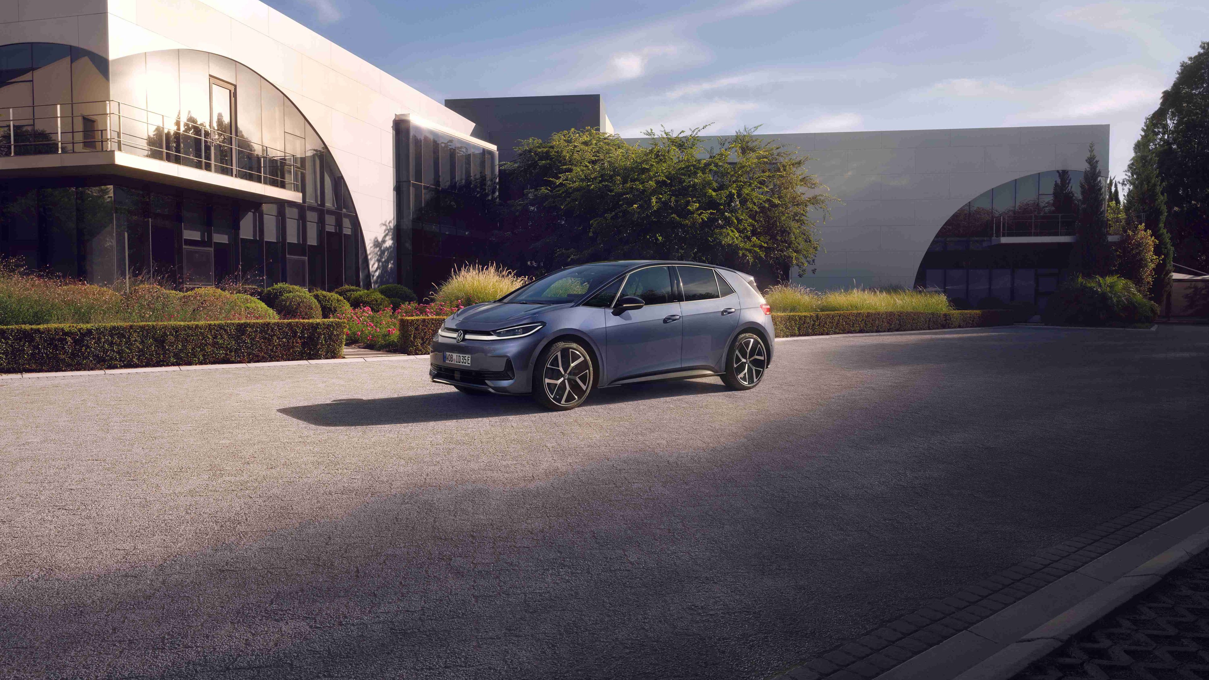 Volkswagen ID.3 Neo zaparkovaný na parkovisku pred modernou verejnou budovou, ktorú osvetľuje slnko.