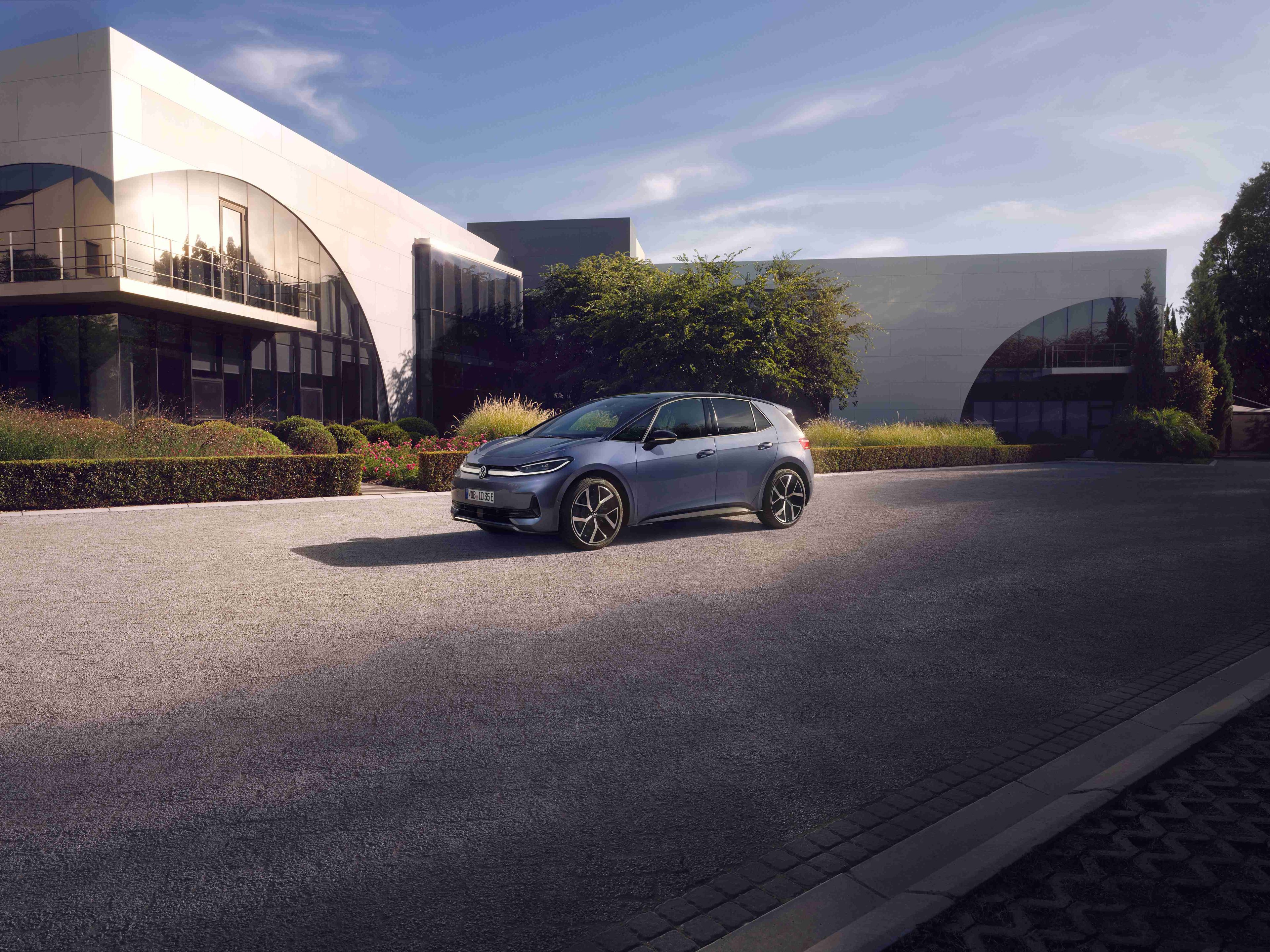 Volkswagen ID.3 Neo zaparkovaný na parkovisku pred modernou verejnou budovou, ktorú osvetľuje slnko.