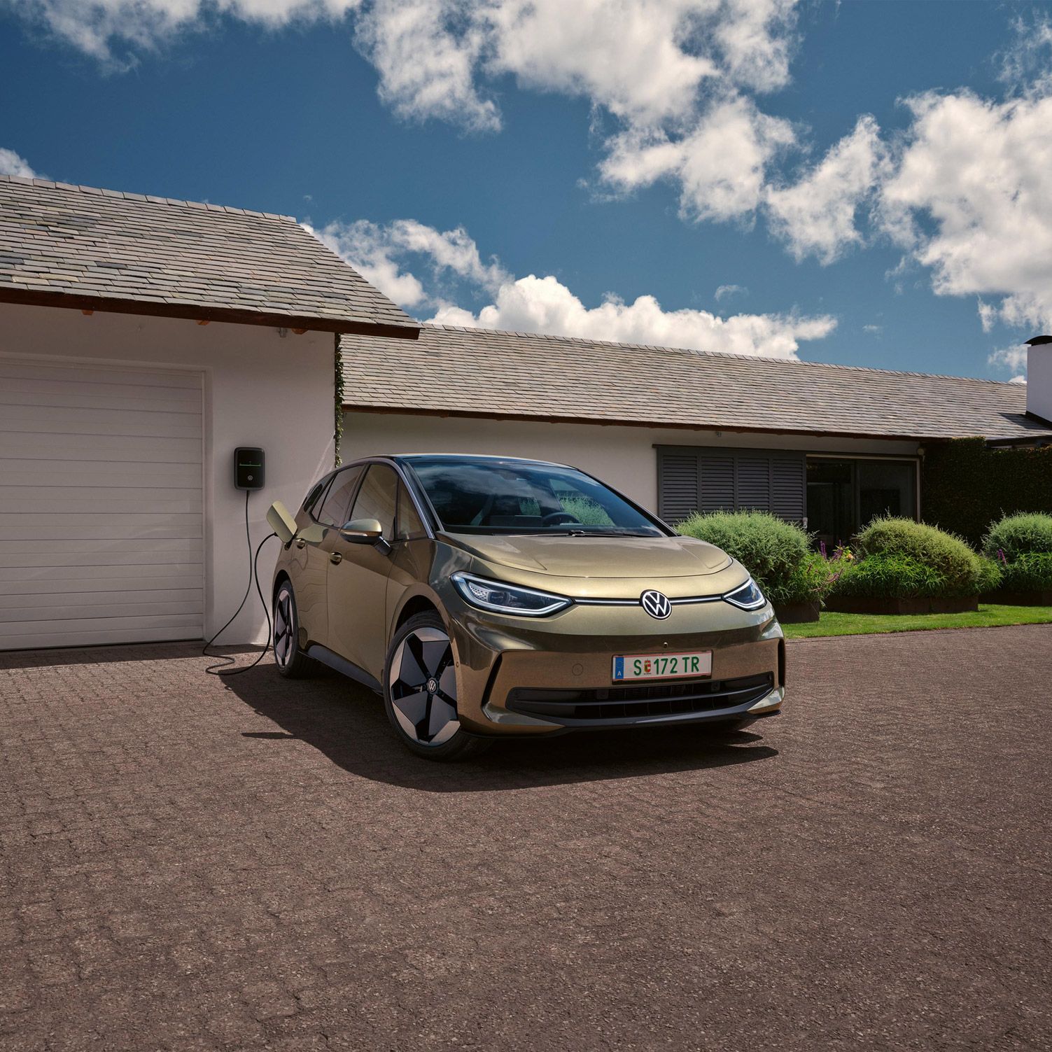 Zaparkované elektrické vozidlo značky Volkswagen nabíjané z domácej nabíjacej stanice. Auto stojí moderným domom za slnečného dňa.