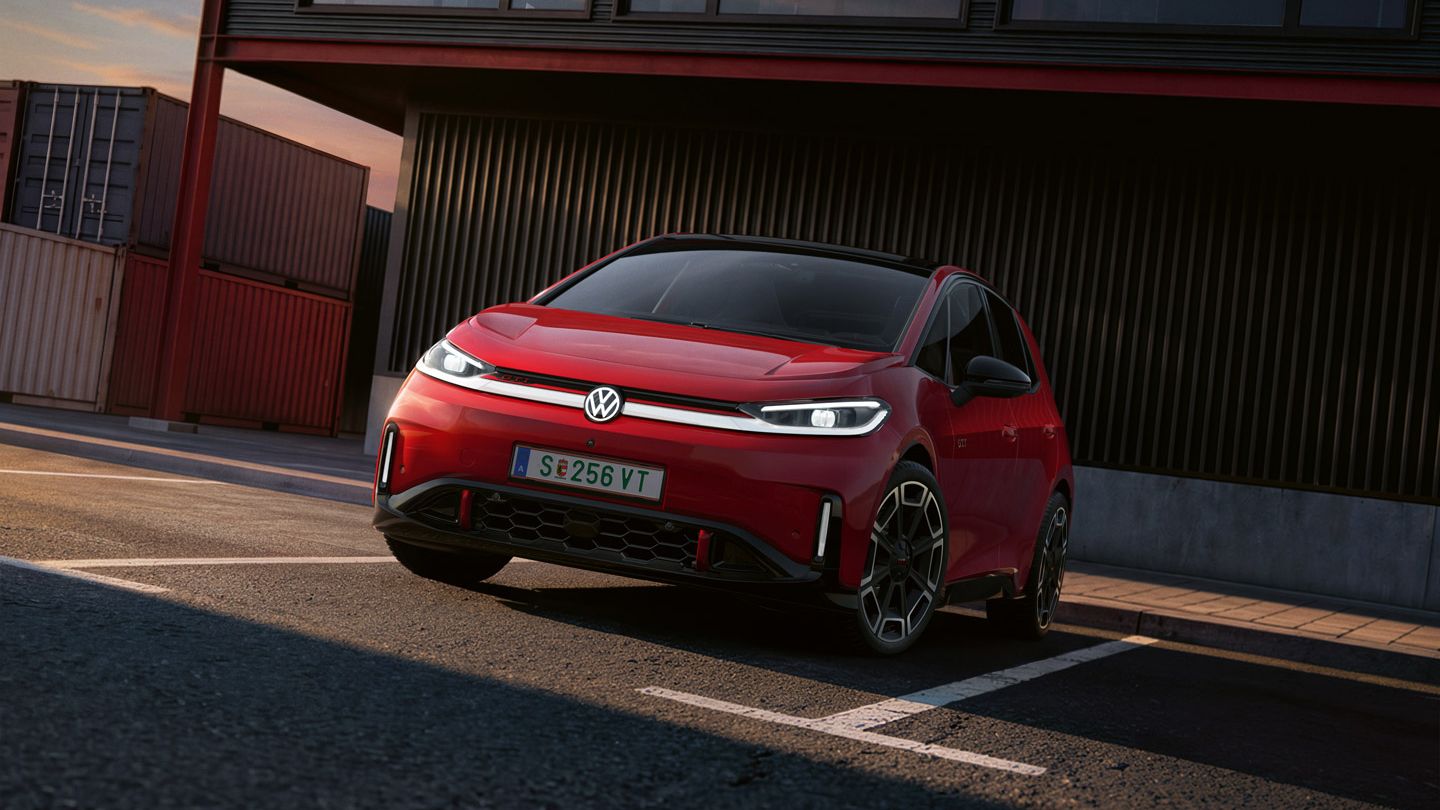 [AI-modified] – Pohľad na predné partie červené VW ID.3 GTI so zapnutými svetlami a rozsvieteným logom pred budovou.
