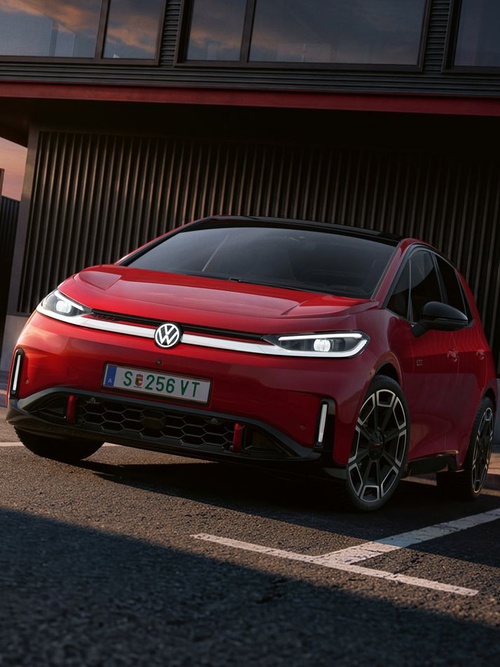 [AI-modified] – Pohľad na predné partie červené VW ID.3 GTI so zapnutými svetlami a rozsvieteným logom pred budovou.