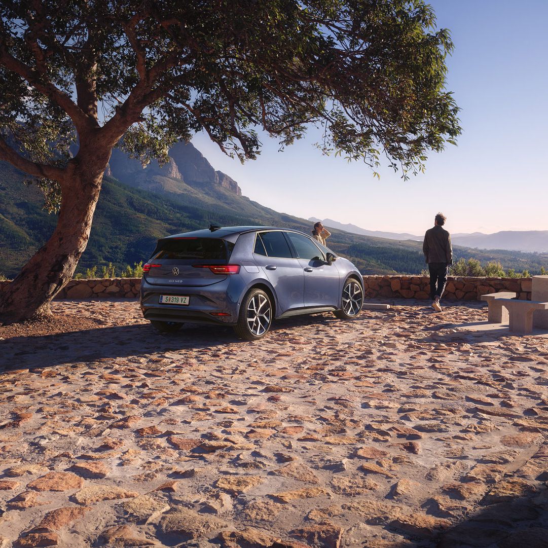 Na parkovisku v horách stojí modrý VW ID.3 Neo, žena a muž si užívajú výhľad.