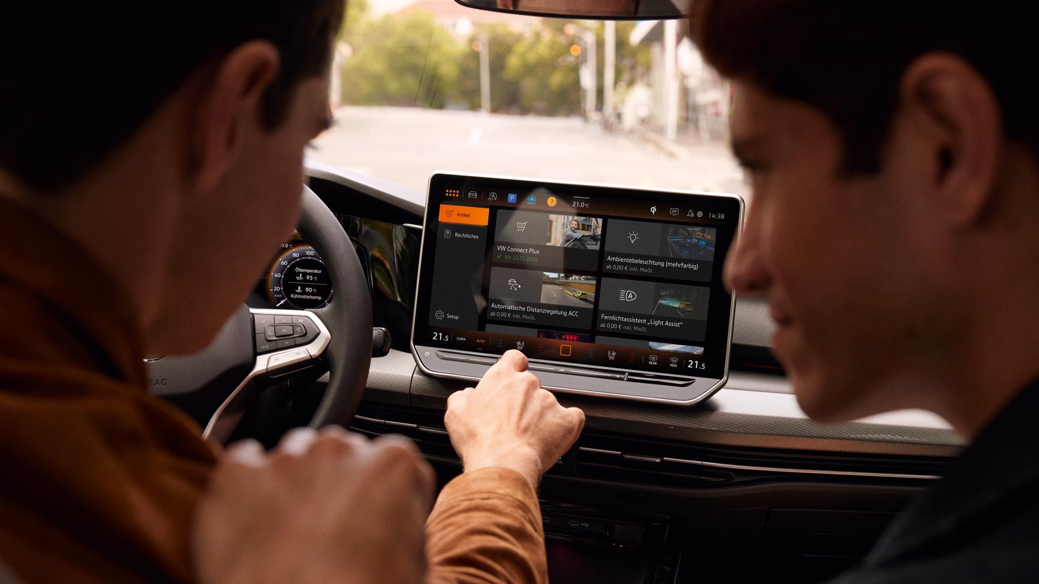 Pohľad do interiéru VW Golf s výhľadom na displej. Muži na sedadle vodiča a spolujazdca ovládajú systém infotainment.