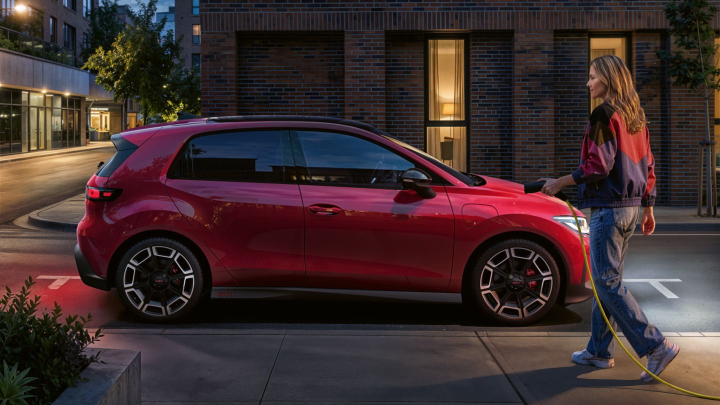 K červenému vozidlu VW ID. Polo GTI, zaparkovanému bokom, sa blíži osoba s nabíjacím káblom na jednosmerný prúd.