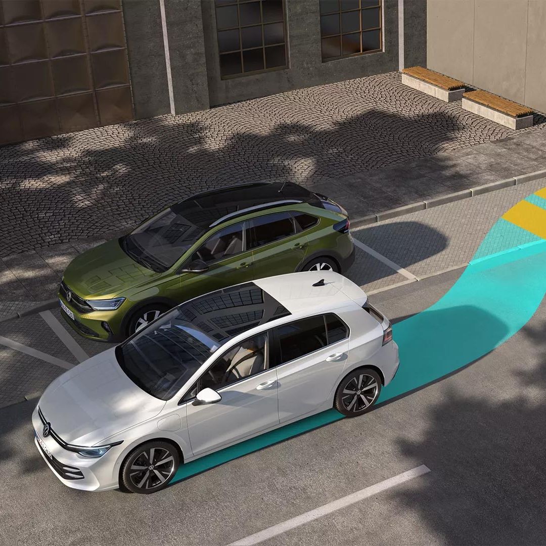Dve vozidlá parkujú pri chodníku a samostatné auto na ceste sa pripravuje na parkovací manéver. Farby na ceste označujú trajektóriu parkovacieho manévru auta. Za vozidlami sú moderné mestské budovy.