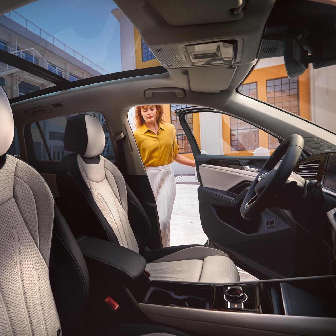 Interiér VW Tiguan. Pohľad z miesta spolujazdca. Cez dvere vodiča nastupuje do vozidla žena. Vidieť tiež panoramatické strešné okno, sedadlá, volant a stredovú konzolu.