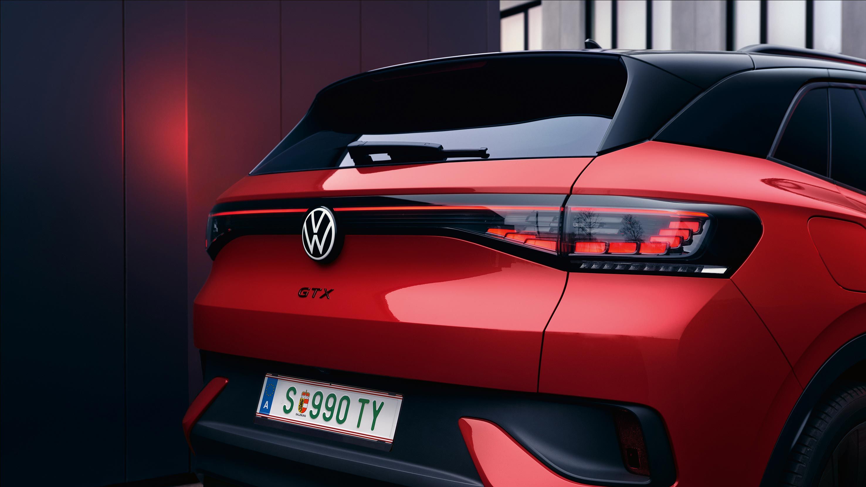 VW ID.4 GTX v červenej farbe. Pohľad na zadné partie vozidla. Zadné svetlá sú zatvorené, svetlo sa odráža v tmavej stene. 