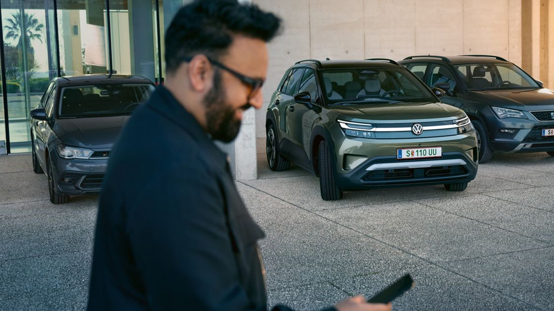 Muž sa pozrie na svoj smartfón, v pozadí VW ID. Cross automaticky zaparkuje na parkovacie miesto.