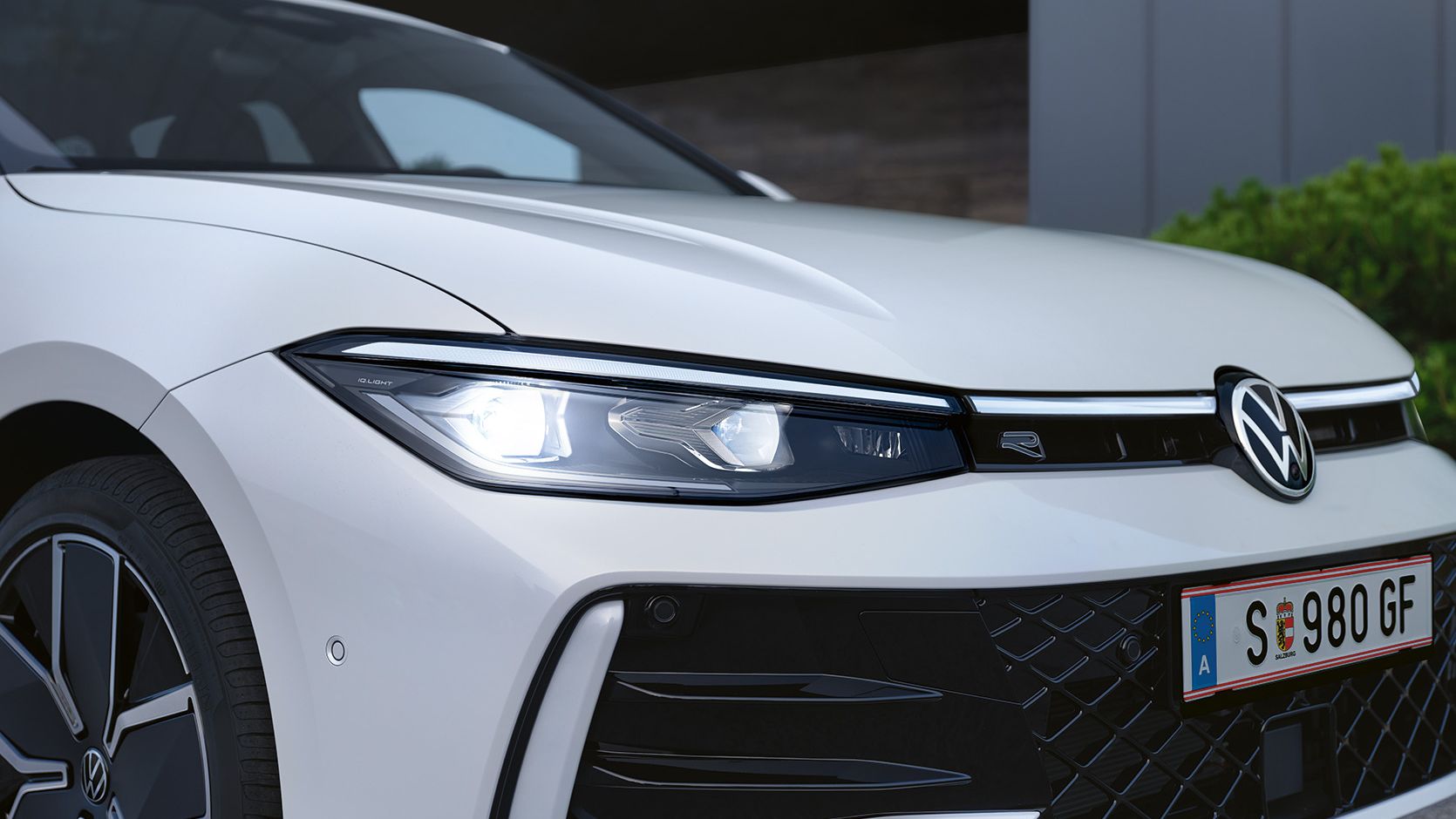 Detail na Matrix LED svetlomety bieleho VW Passat, kde vidieť tiež predný nárazník, koleso s moderným diskom a celé predné partie vozidla. Bočný pohľad spredu.