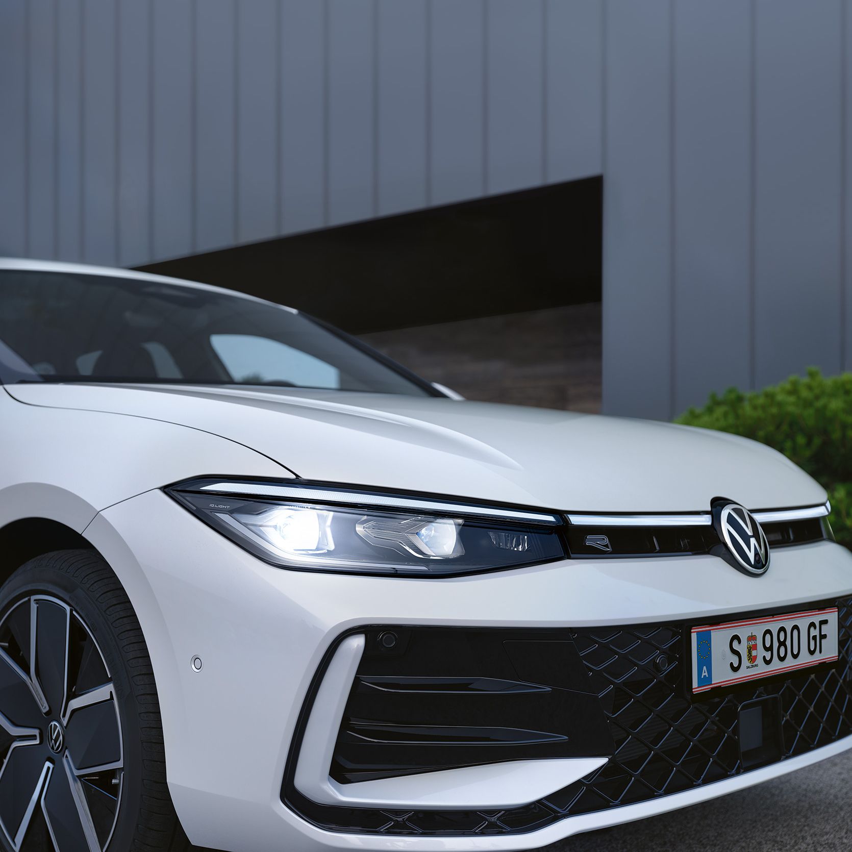 Detail na Matrix LED svetlomety bieleho VW Passat, kde vidieť tiež predný nárazník, koleso s moderným diskom a celé predné partie vozidla. Bočný pohľad spredu.