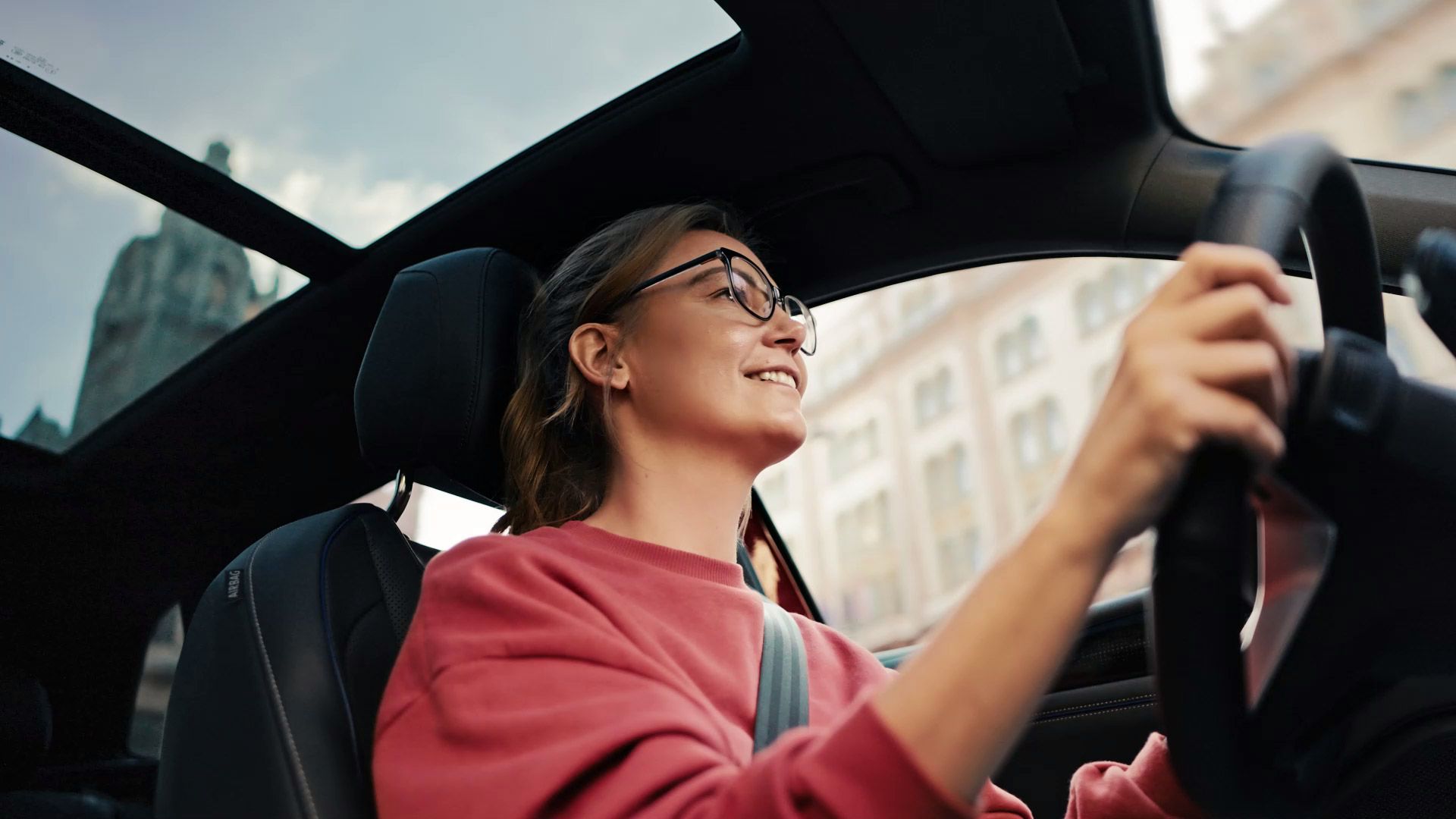 Vodička sedí za volantom vozidla Volkswagen, nad ňou je cez panoramatickú strechu viditeľné mestské prostredie.