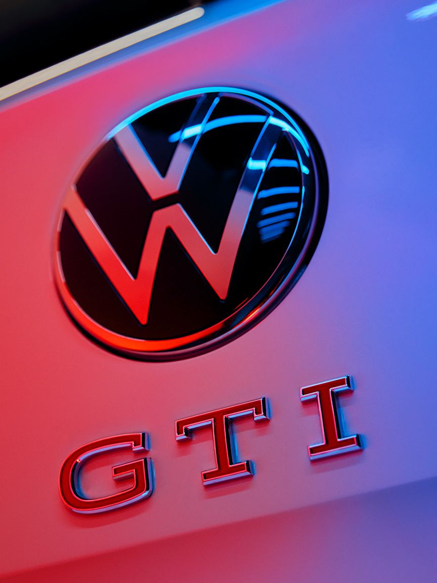 Logo Volkswagen GTI na zadných dverách osvetlené modro červeným svetlom. V dolnej časti je nápis GTI. Okolo loga a nápisu sú rozmazané svetelné pruhy.