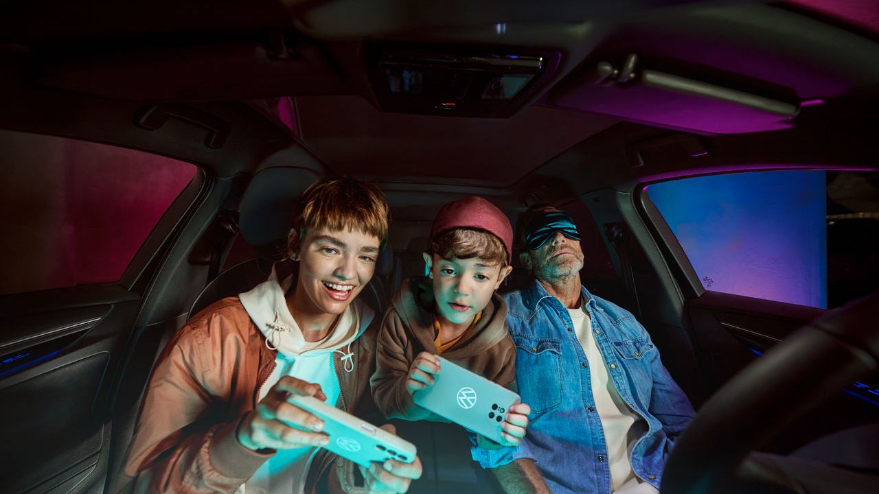 Otec s dvoma deťmi vo vozidle Volkswagen, deti sa hrajú s AirConsole.