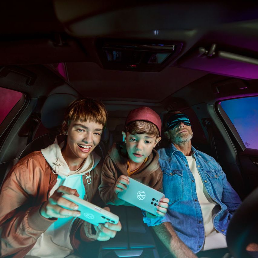 Otec s dvoma deťmi vo vozidle Volkswagen, deti sa hrajú s AirConsole.