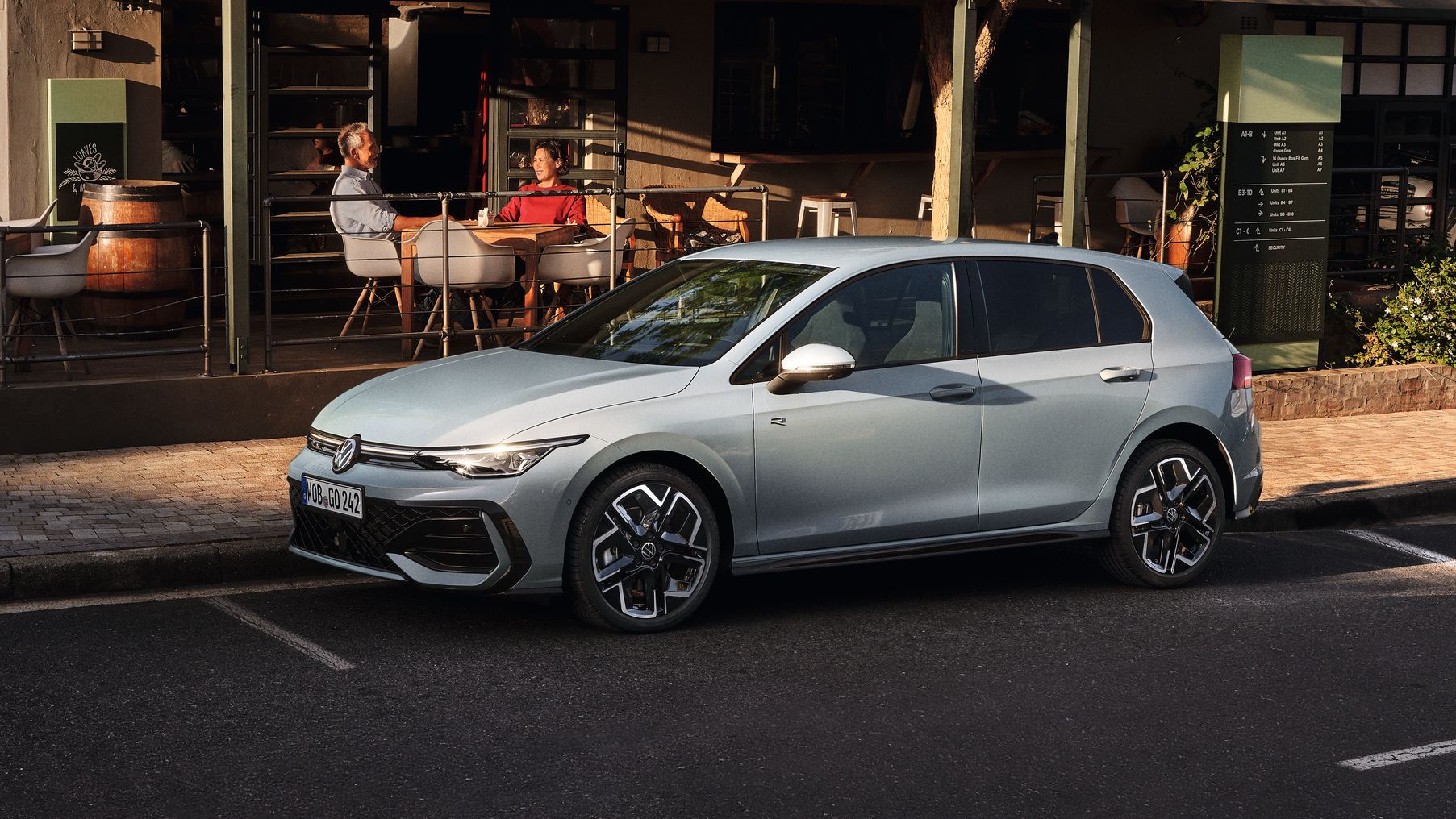 Biely Golf R-Line zaparkovaný na parkovacom mieste na ceste pred reštauráciou. Za vozidlom je reštaurácia a na terase sedia zákazníci.