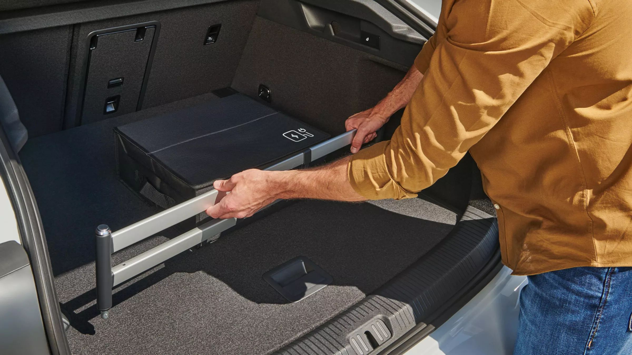 Muž upevňuje zásuvný modul do batožinového priestoru od príslušenstva VW v batožinovom priestore vozidla VW ID.7