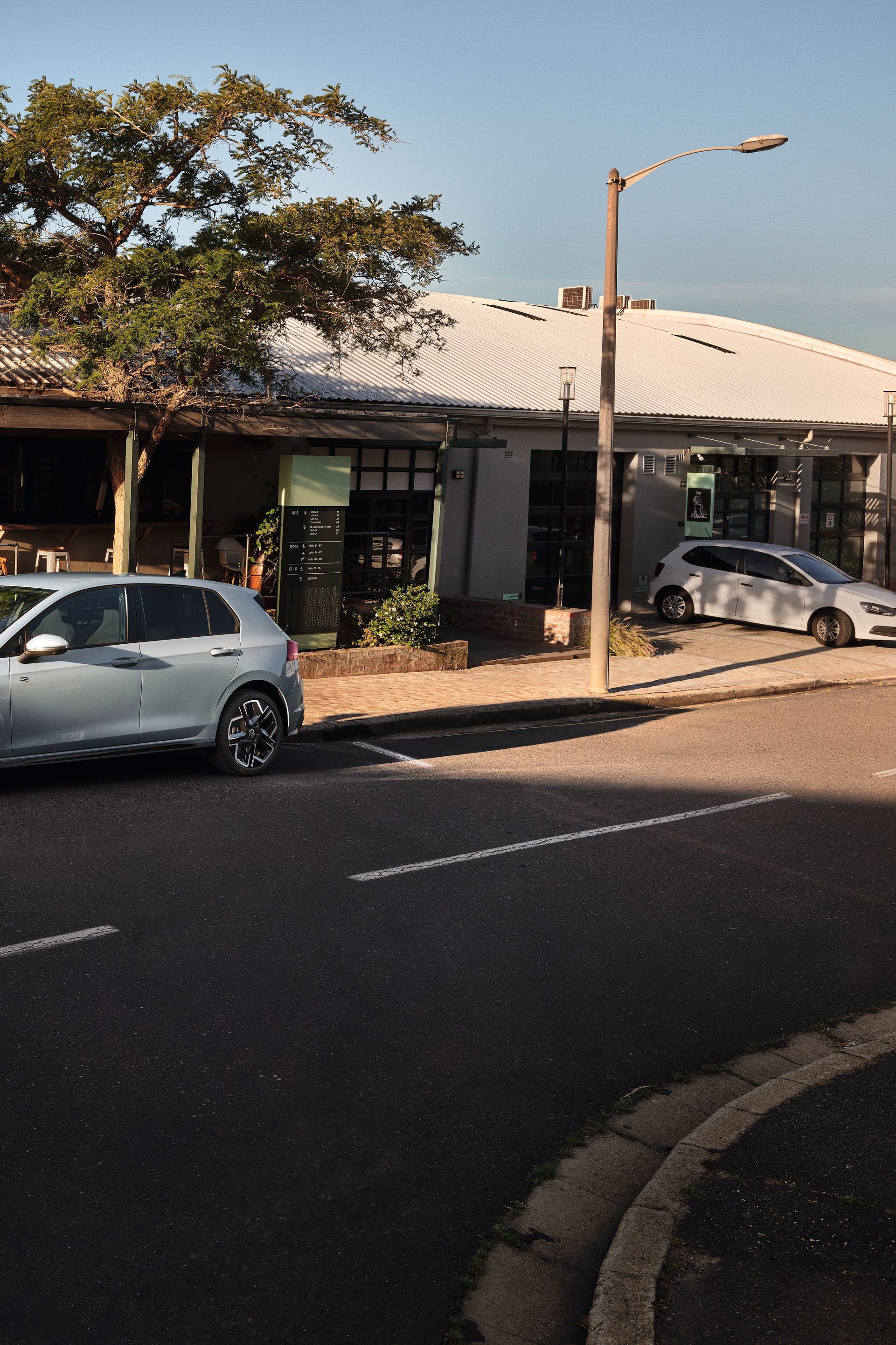 Biely Golf R-Line zaparkovaný na parkovacom mieste na ceste pred reštauráciou. Za vozidlom je reštaurácia a na terase sedia zákazníci.