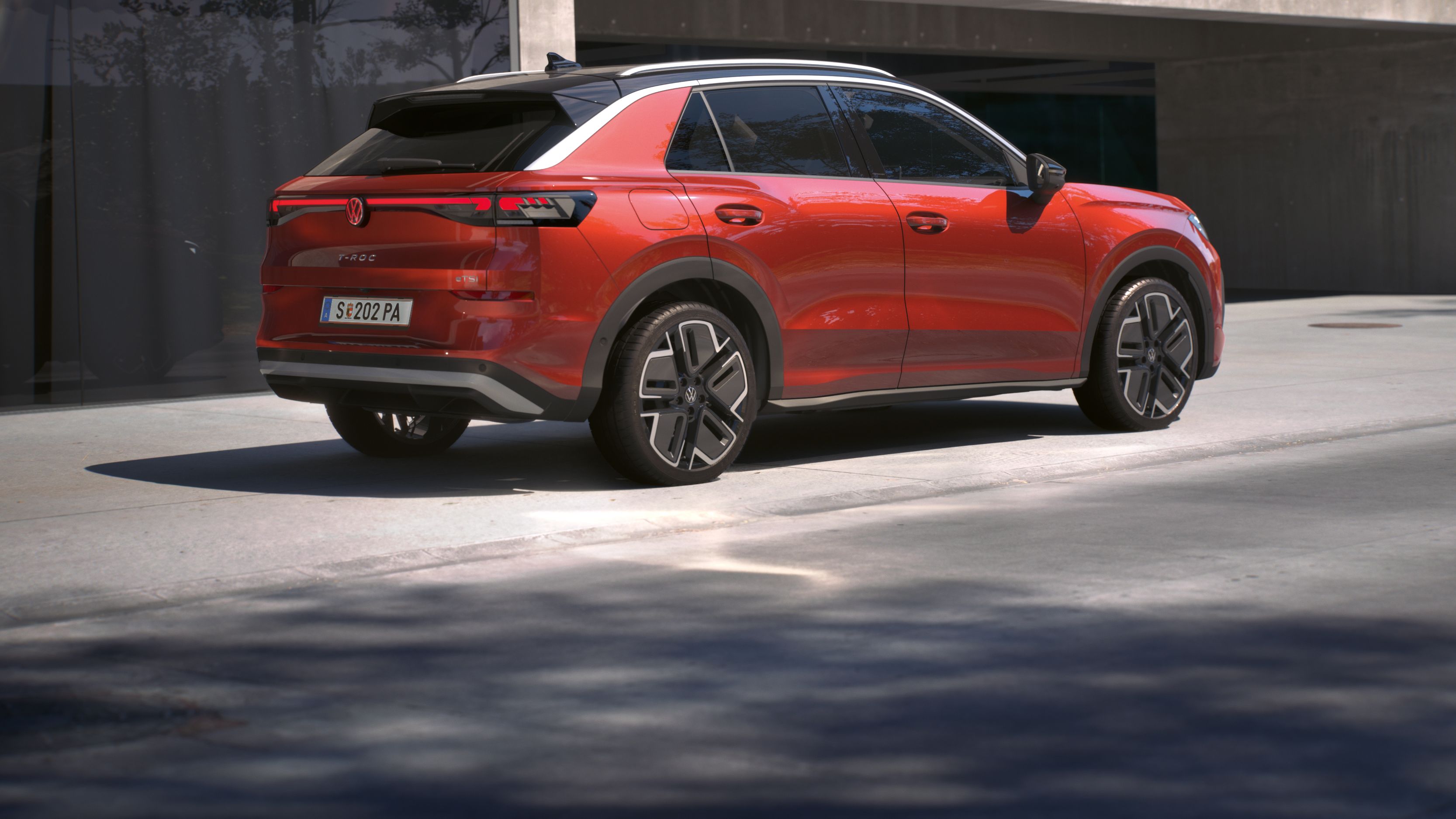 Pohľad na zadné partie červeného modelu T-Roc Style zboku, ktorý je zaparkovaný pre budovou.