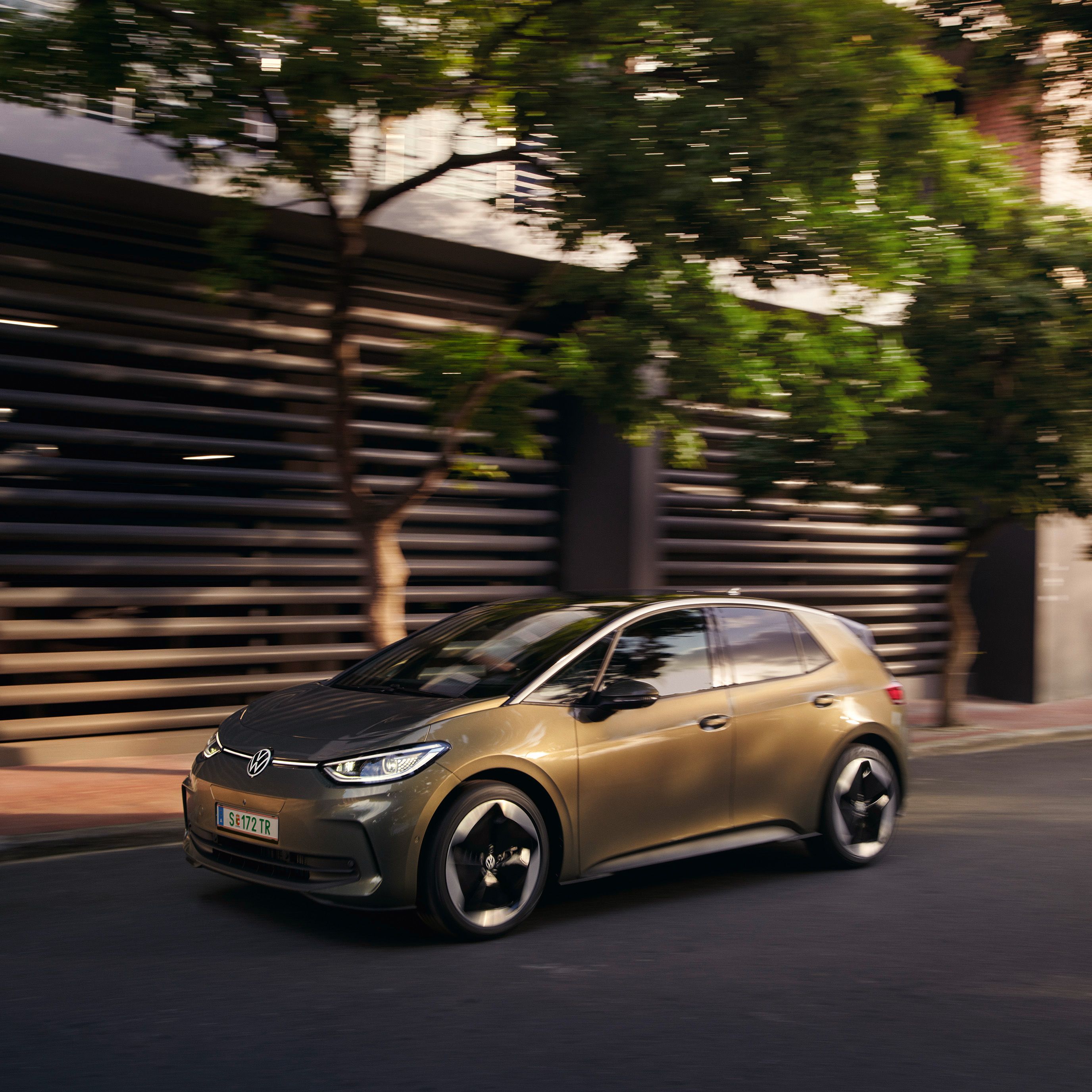 VW ID.3 v olivovo zelenej farbe jazdí v meste okolo modernej budovy.