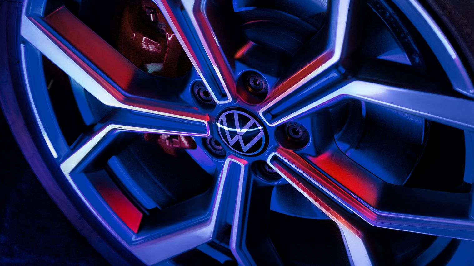 Detailný záber na koleso automobilu Volkswagen s moderným dizajnom disku osvetleným modrým a červeným svetlom.