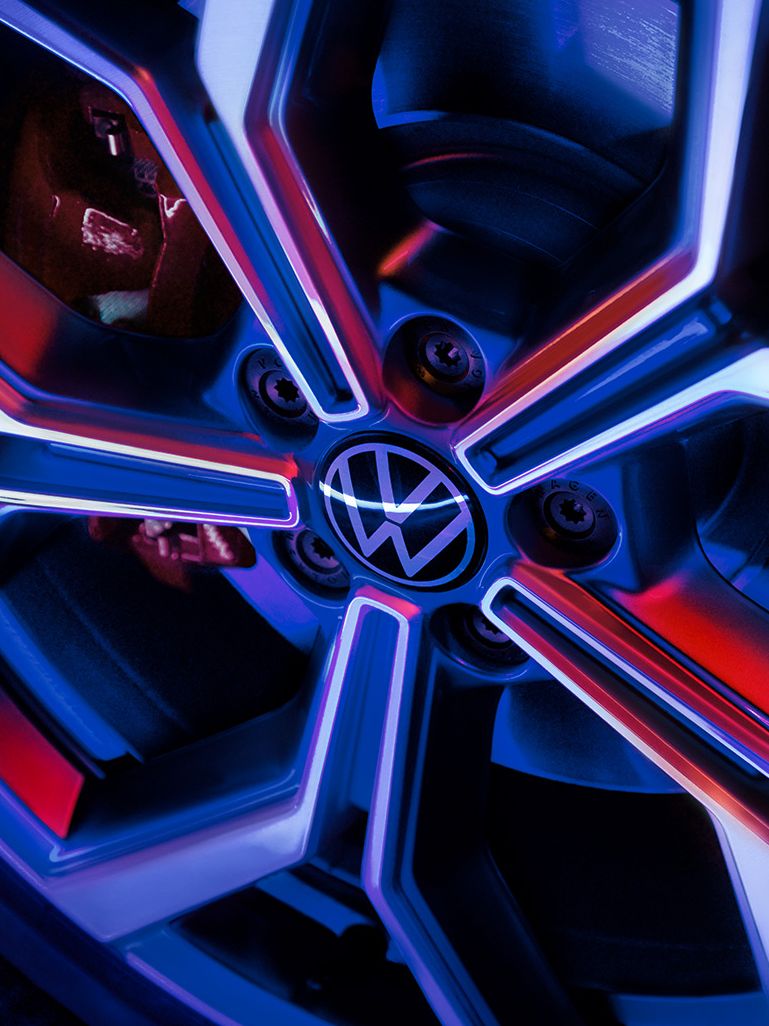 Detailný záber na koleso automobilu Volkswagen s moderným dizajnom disku osvetleným modrým a červeným svetlom.