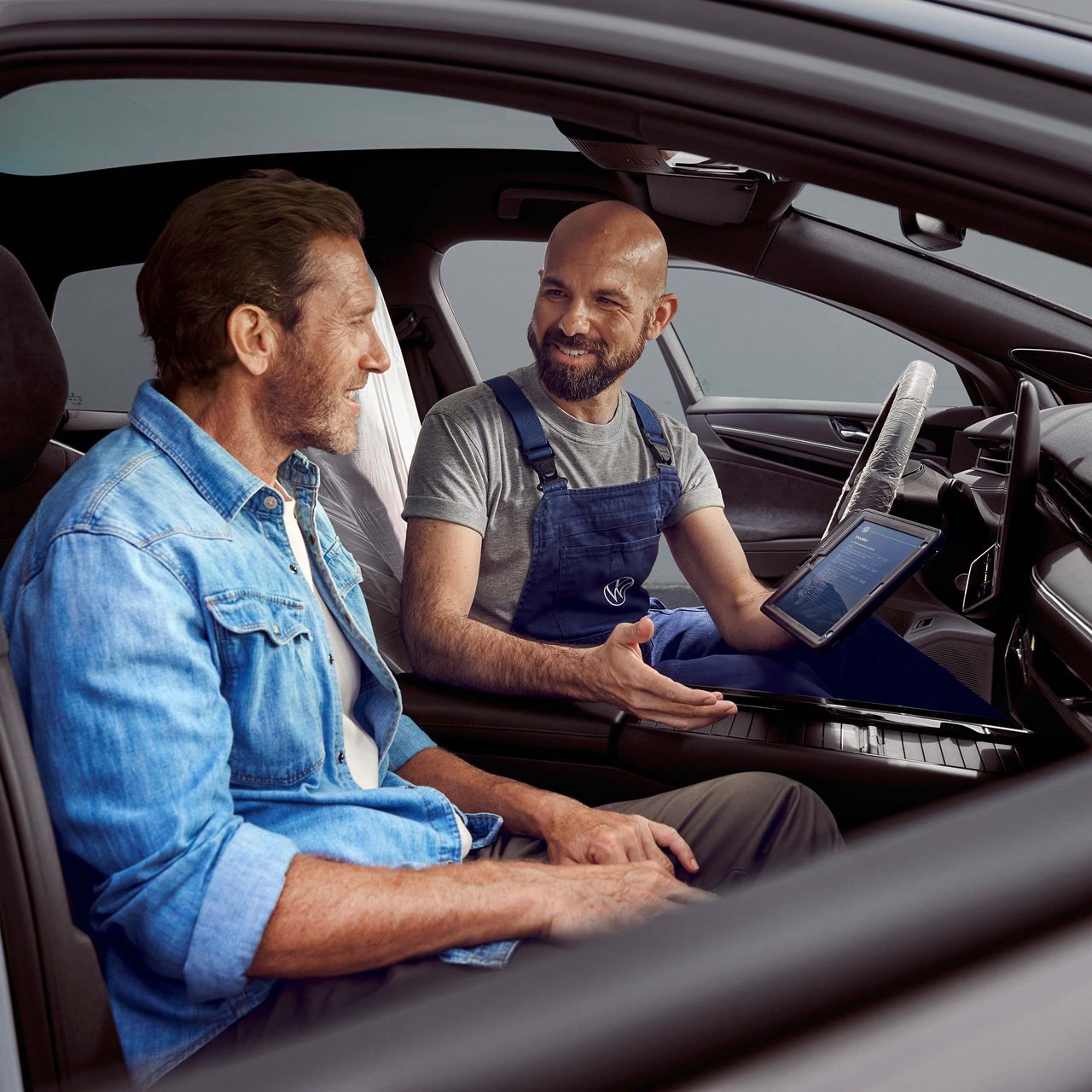 Zákazník sedí v aute, servisný technik spoločnosti VW mu niečo vysvetľuje na tablete.
