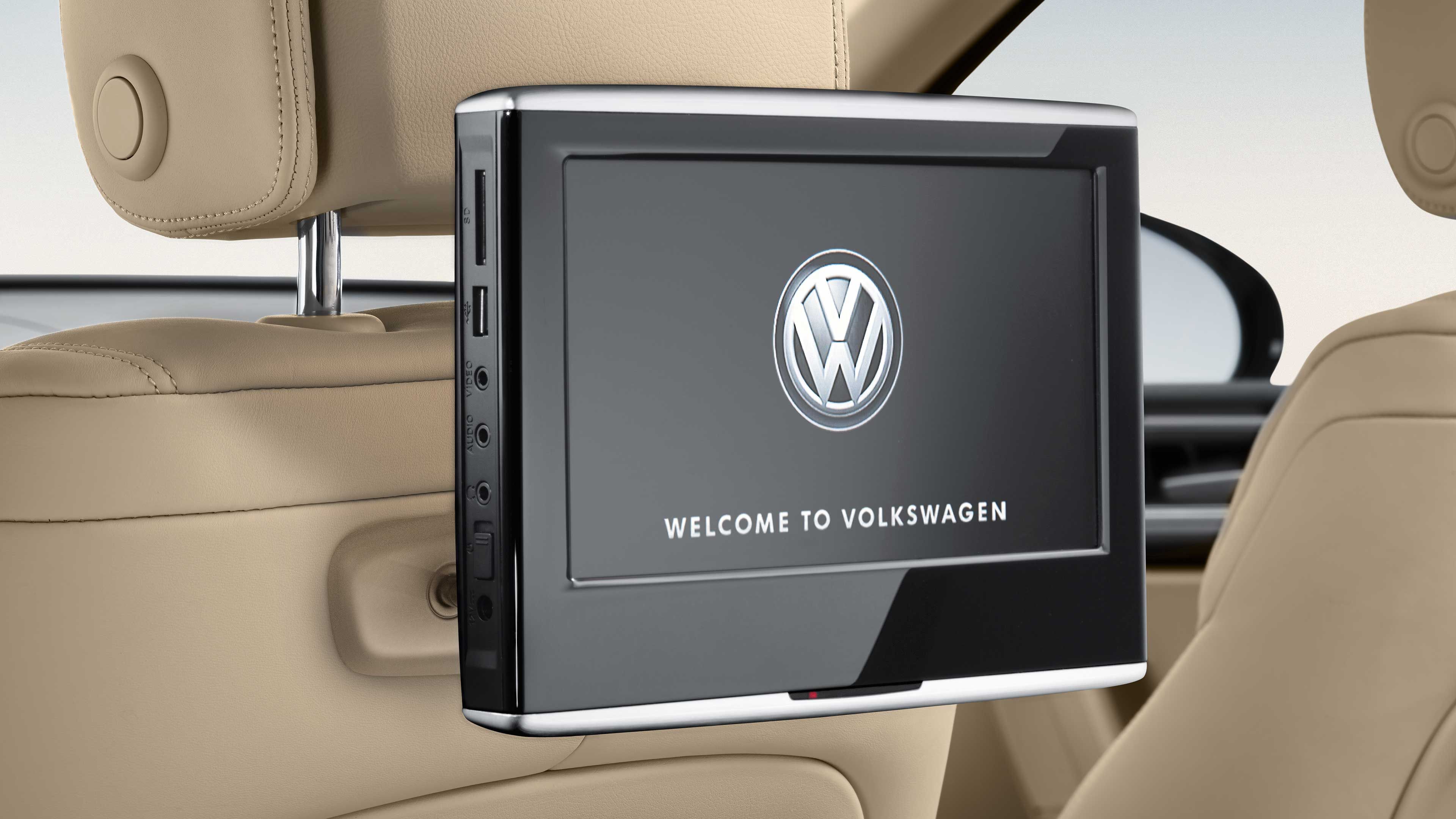 Displej upevnený na zadnej strane predného sedadla automobilu značky Volkswagen. Na obrazovke je zobrazené logo Volkswagen s textom "Welcome to Volkswagen". Okolo je interiér vozidla s krémovým čalúnením.