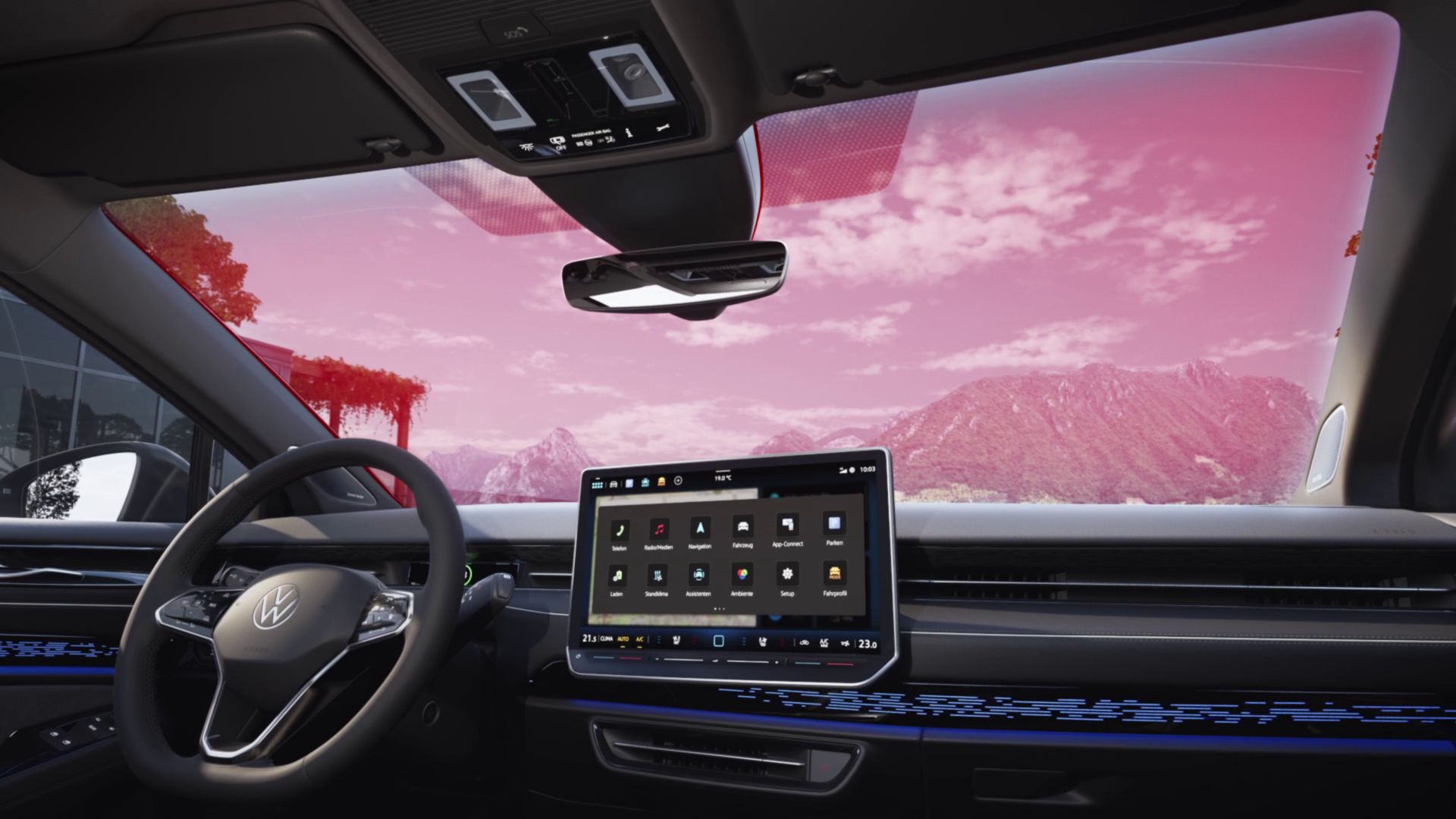 Interiér moderného auta s veľkým digitálnym displejom v stredovej konzole. Vidieť volant a čelné sklo, cez ktoré je vidieť krajinu s horami a červenou oblohou.