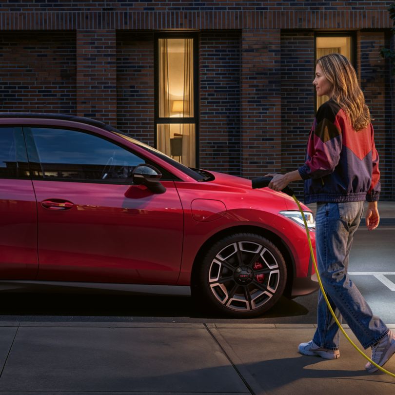 K červenému vozidlu VW ID. Polo GTI, zaparkovanému bokom, sa blíži osoba s nabíjacím káblom na jednosmerný prúd.