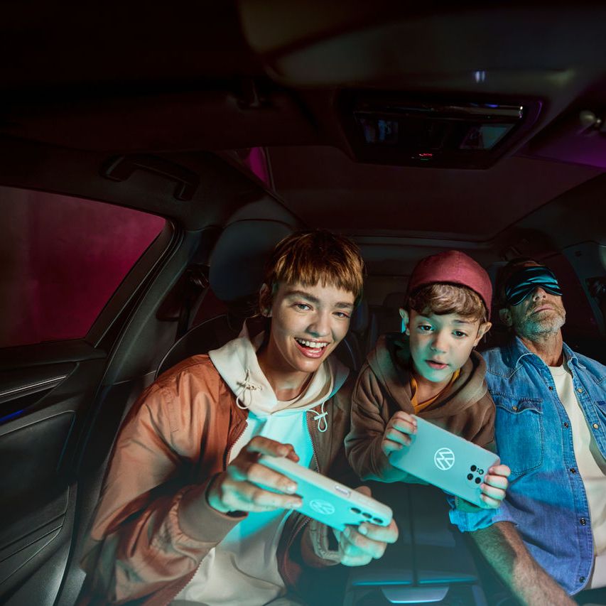 Otec s dvoma deťmi vo vozidle Volkswagen, deti sa hrajú s AirConsole.