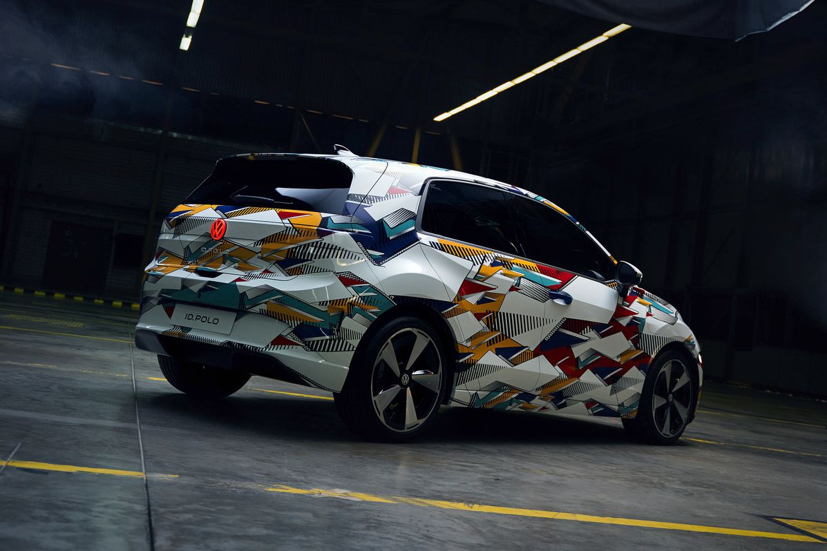 Fotografia zobrazuje auto vo futuristickej hale s vysokým stropom. Vozidlo má moderný dizajn s pestrofarebnou kamuflážou.