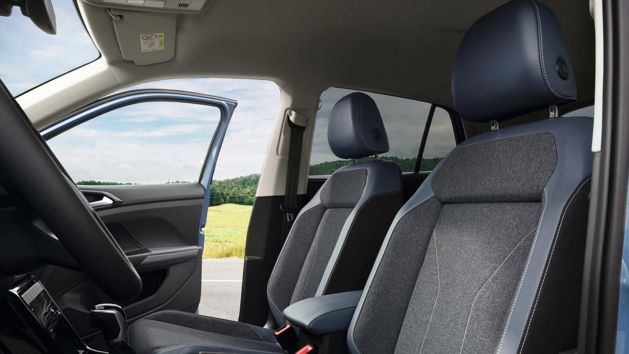 Pohľad na predné sedadlá s otvorenými prednými dverami spolujazdca, cez ktoré je výhľad na cestu, lúku a les.