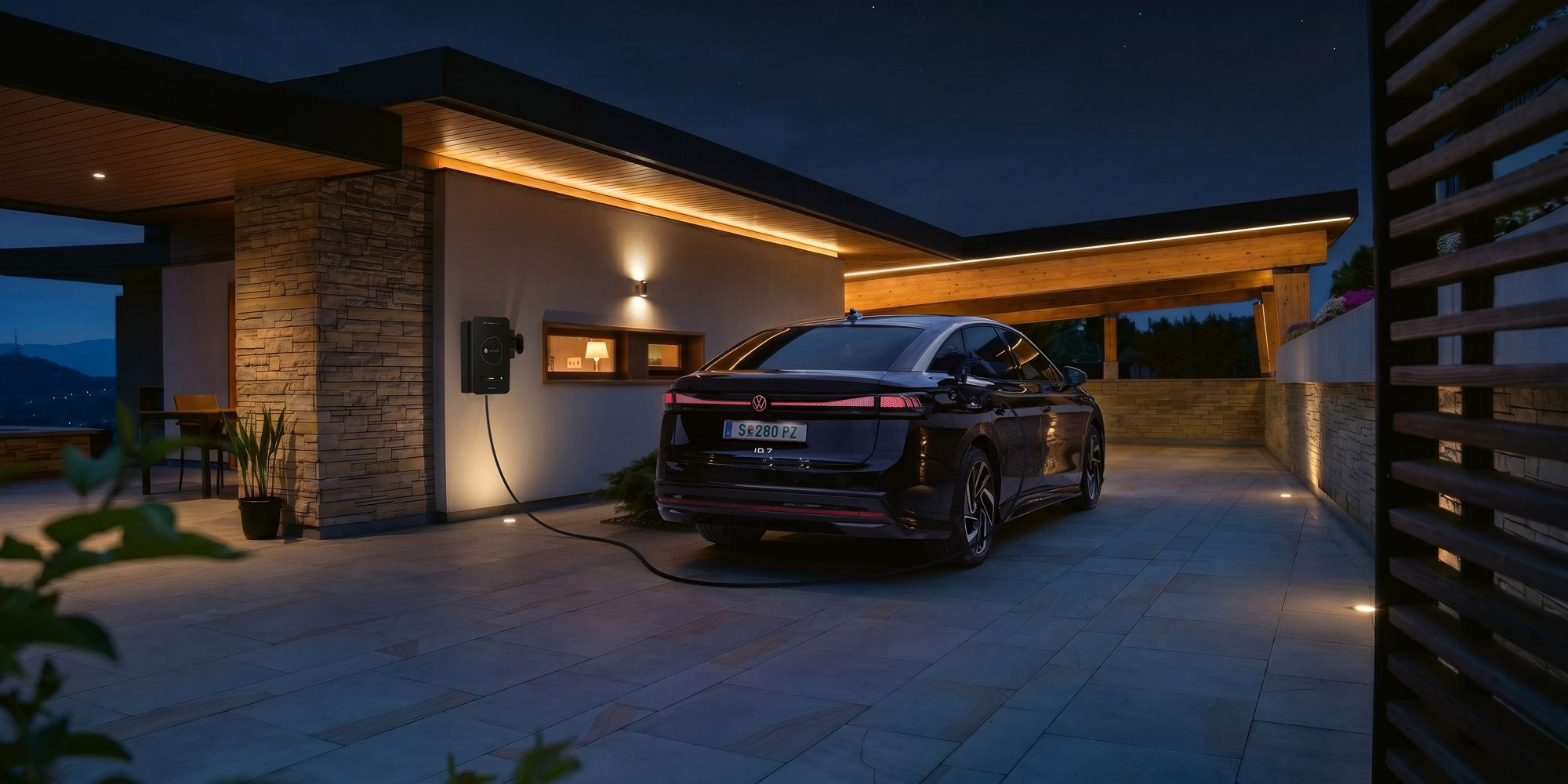 Čierne elektrické auto je zaparkované na príjazdovej ceste moderného domu v noci a je pripojené k domácej nabíjacej stanici. Teplé, nepriame svetlo na fasáde a prístrešku osvetľuje scénu. V pozadí sa črtajú kopce za súmraku.