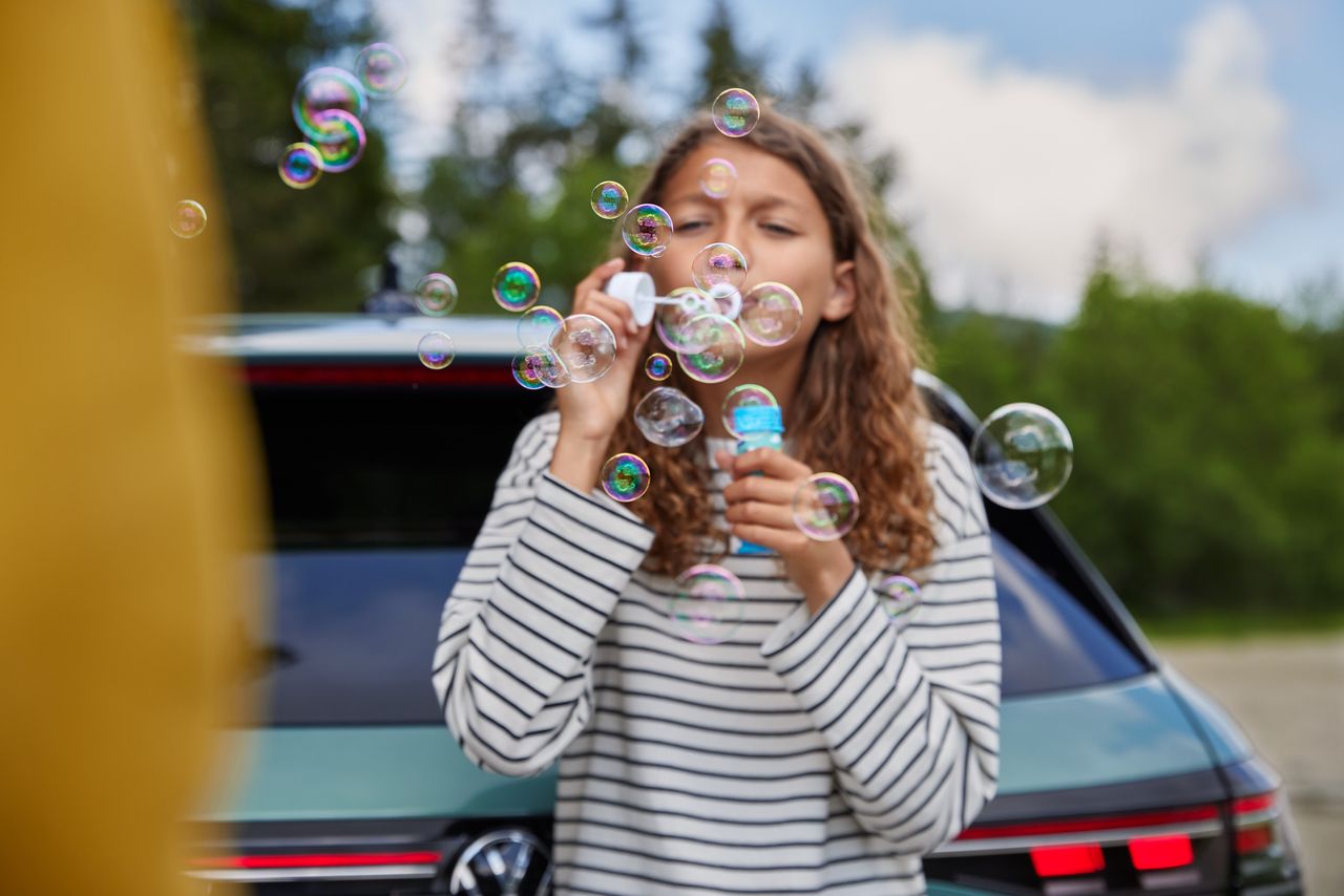 Dieťa stojí pred vozidlom Volkswagen a fúka do vzduchu mydlové bubliny.