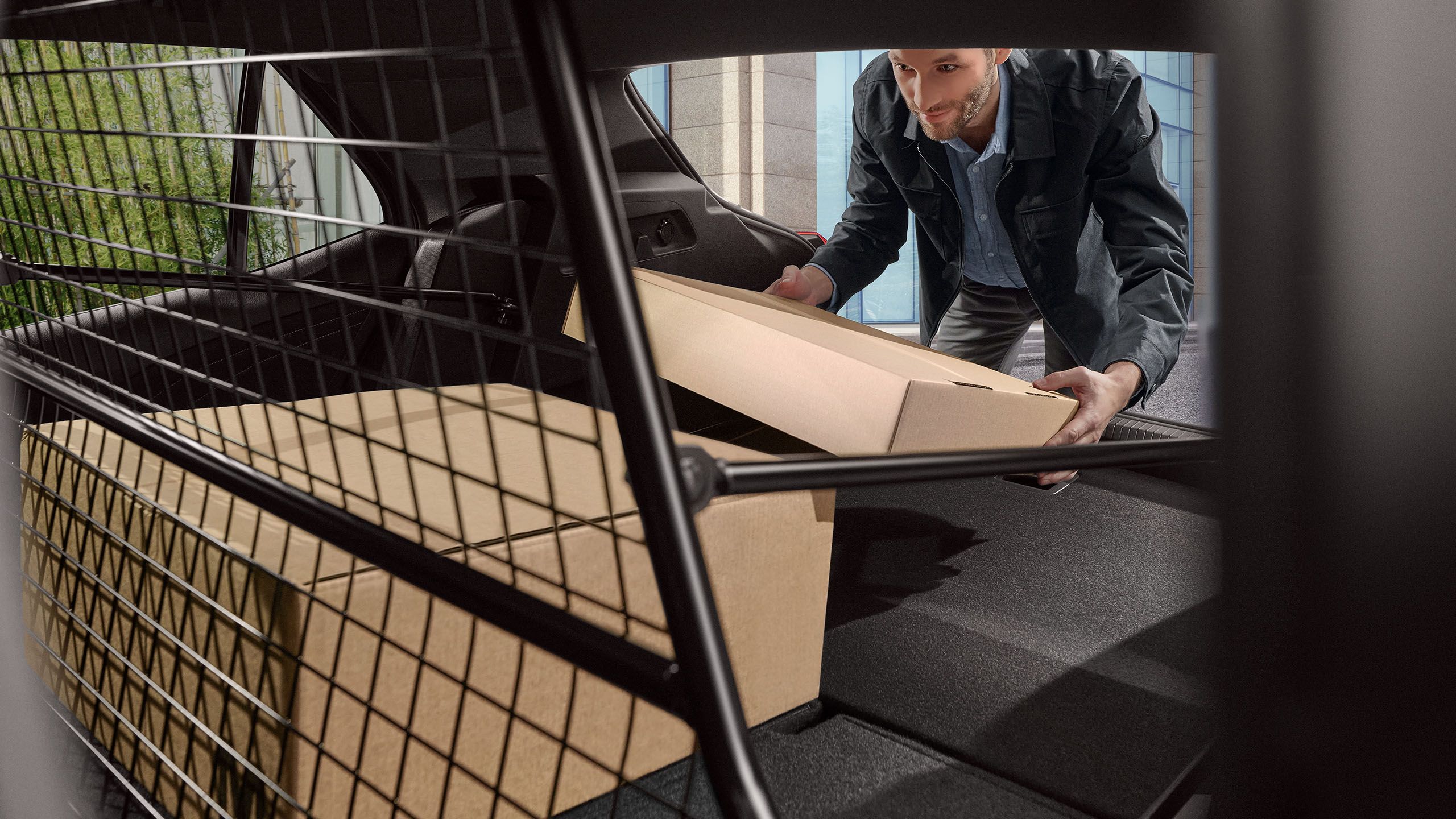  Muž nakladá batožinový priestor boxmi, v centre pozornosti je deliaca mriežka batožinového priestoru od VW Accessories