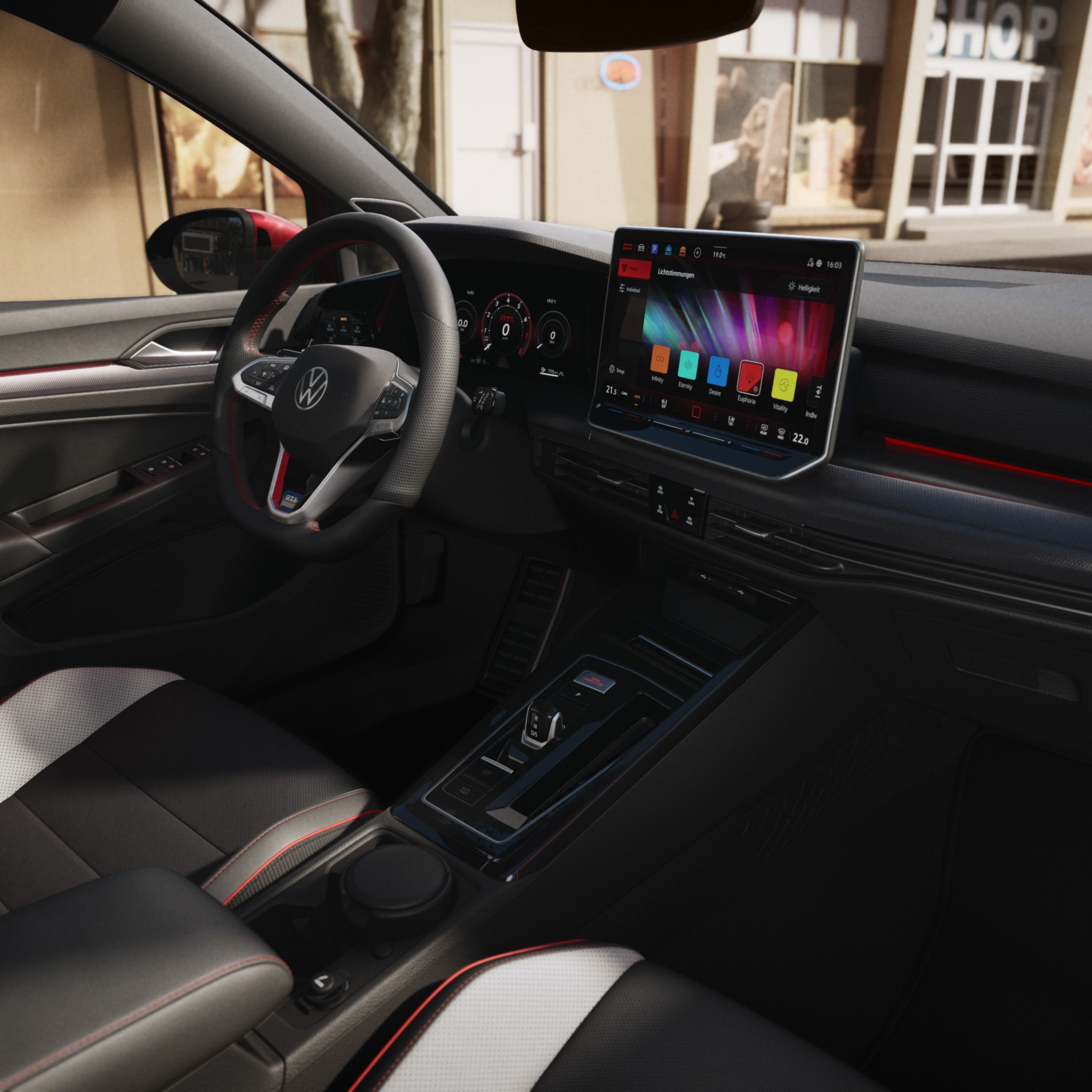 Pohľad do interiéru VW Golf GTI zo sedadla spolujazdca. Dobre viditeľné sedadlo vodiča v dvojfarebnom čierno-bielom čalúnení, volant, digitálny prístrojový panel, displej systému infotainment, palubná doska čiernej farby, obklad dverí. Cez čelné sklo vidieť svetlú budovu.