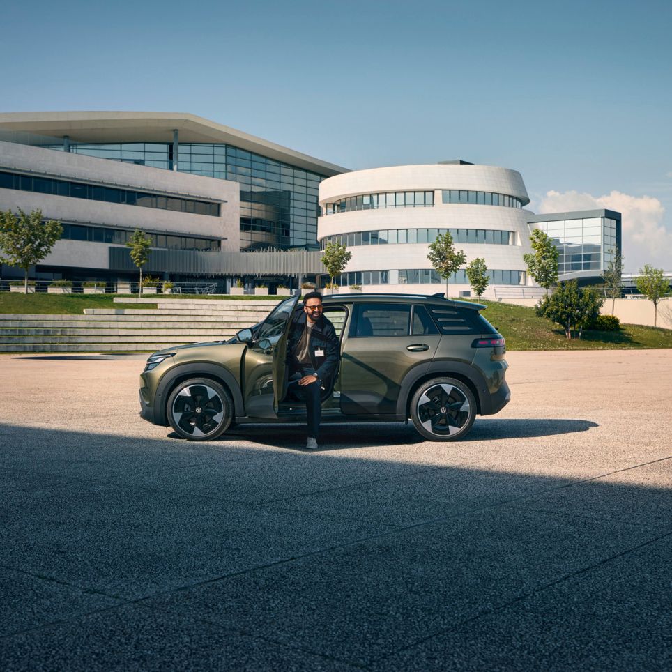 Muž vystupuje z dverí vodiča vozidla VW ID. Cross, ktoré stojí pred modernou viacposchodovou firemnou budovou.