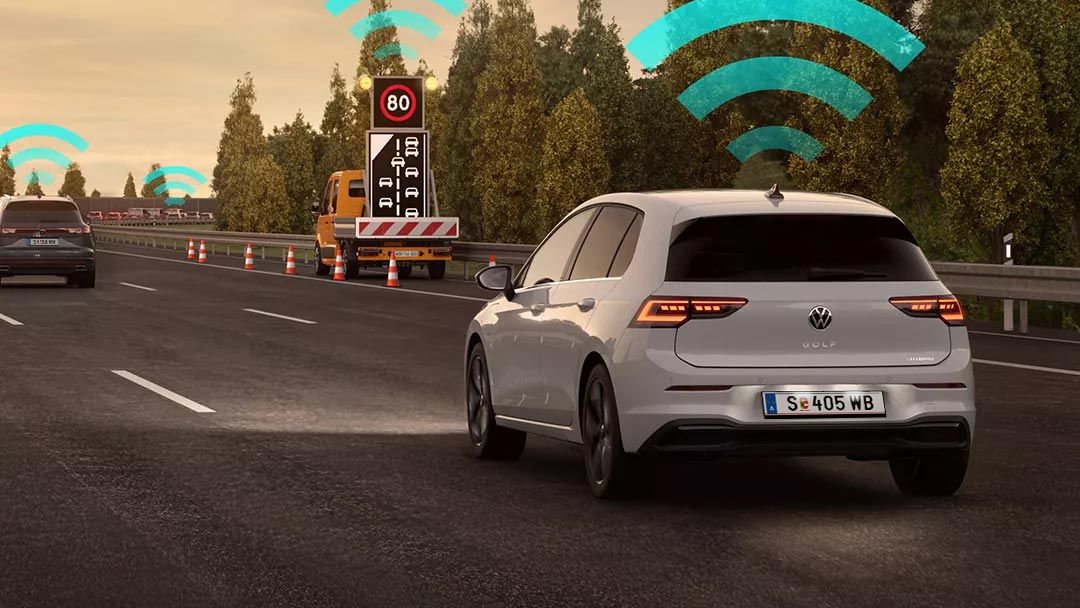Vozidlo VW Golf jazdí v jazdnom pruhu na diaľnici. Nad autom sú ikony znázorňujúce pripojenie na internet. V pozadí je nákladné auto a stromy.