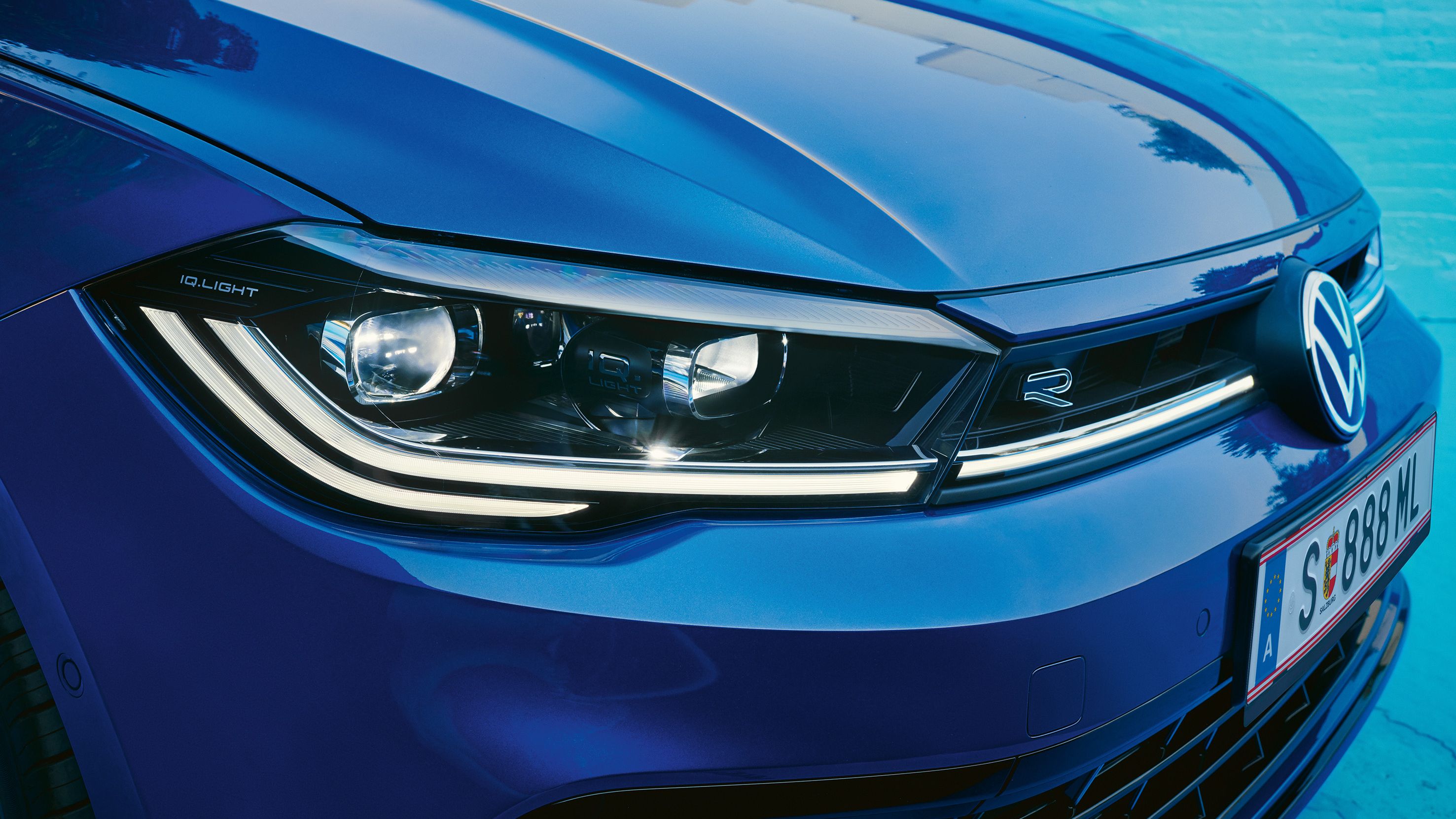 Detailný pohľad na predné svetlá modrého vozidla značky Volkswagen. Svetlá sú LED s moderným dizajnom.