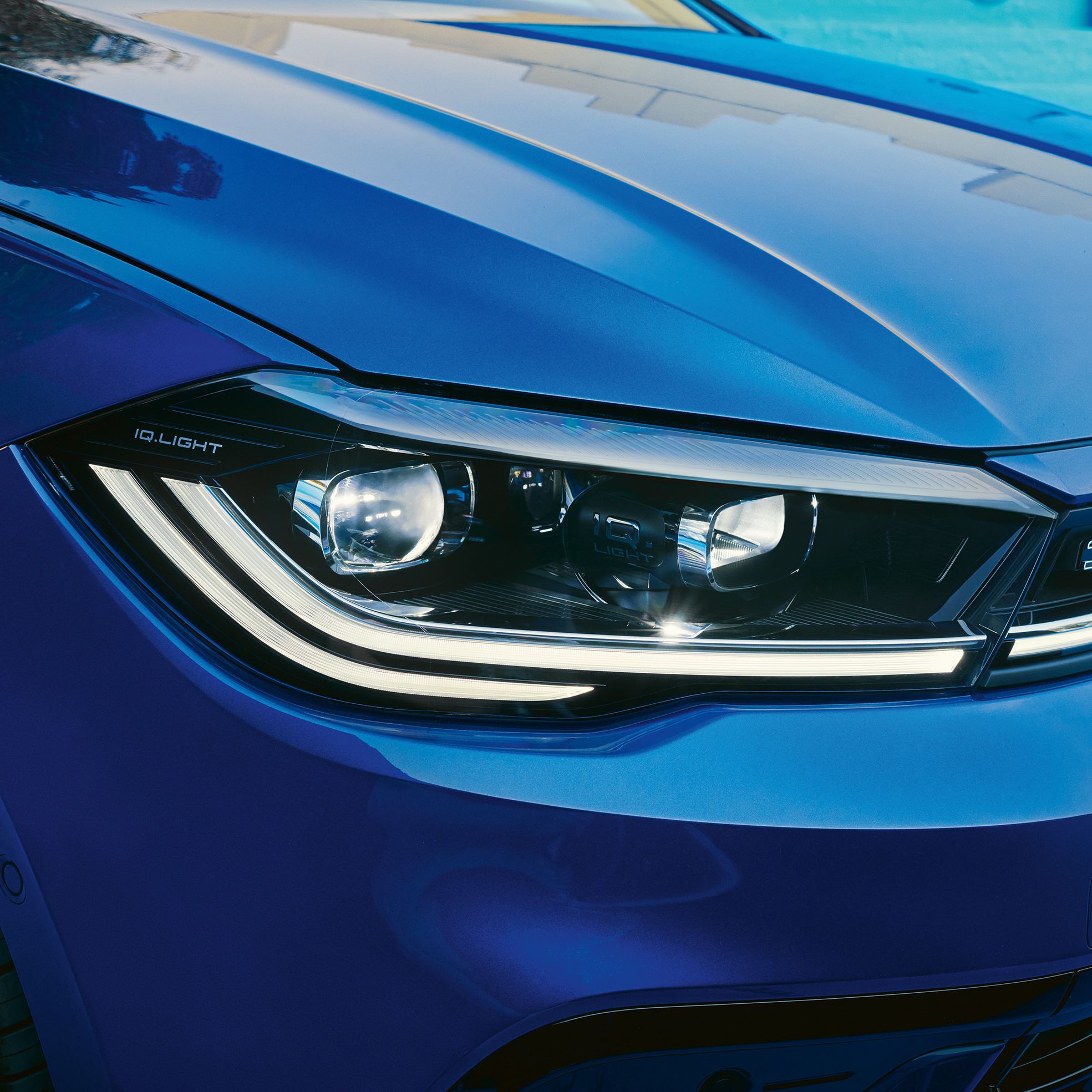 Detailný pohľad na predné svetlá modrého vozidla značky Volkswagen. Svetlá sú LED s moderným dizajnom.