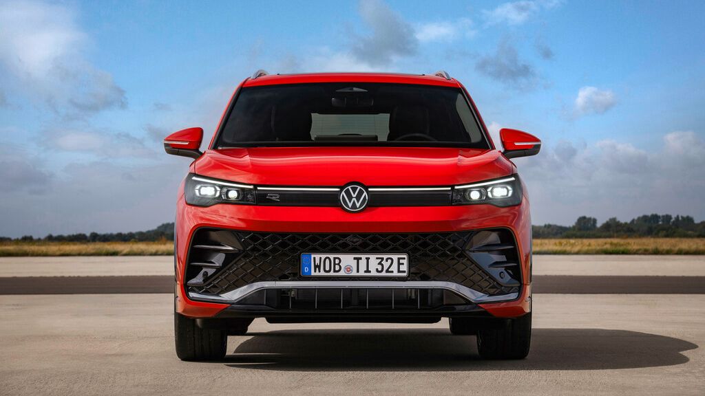 Červený VW Tiguan stojí na otvorenom priestranstve. Pohľad na vozidlo spredu. Pozadie tvorí modrá obloha s niekoľkými oblakmi a zeleň.