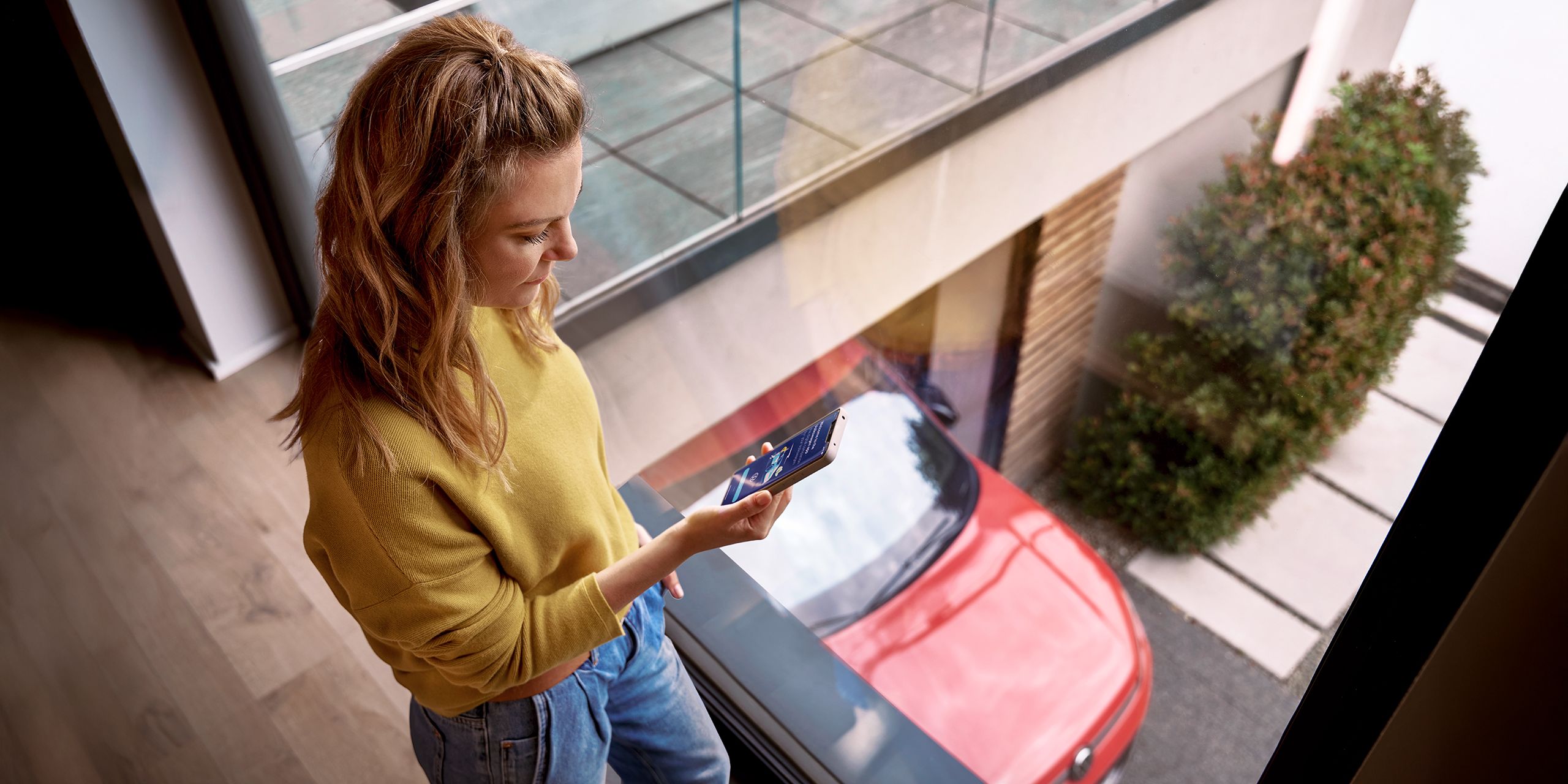 Žena sa prihlasuje do zákazníckeho portálu myVolkswagen na svojom smartfóne, v pozadí je auto značky VW.