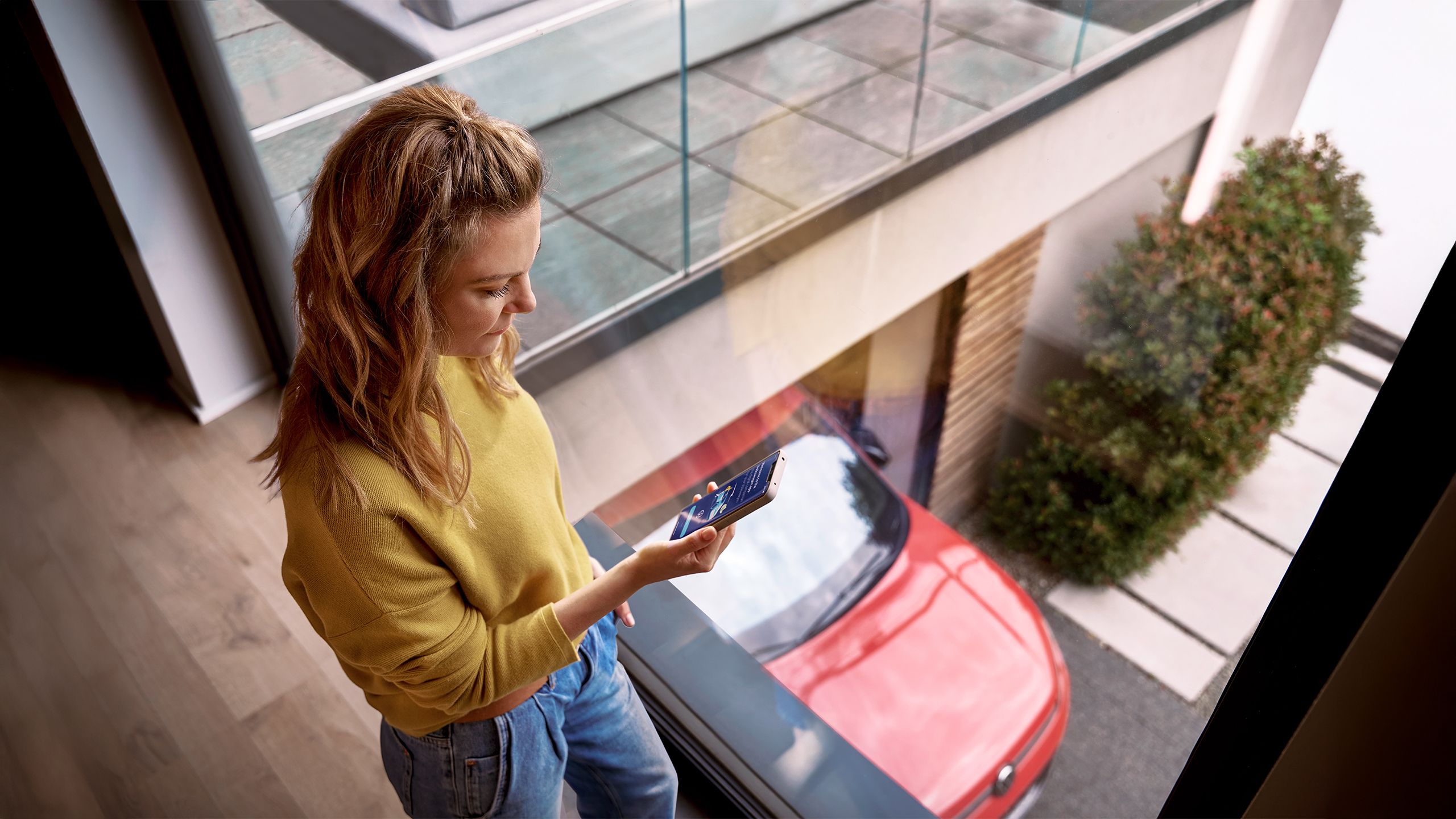 Žena sa prihlasuje do zákazníckeho portálu myVolkswagen na svojom smartfóne, v pozadí je auto značky VW.