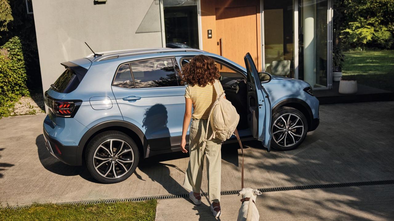 Dievča so psom kráča smerom k modrému VW T-Cross na príjazdovej ceste. Dvere spolujazdca sú otvorené.