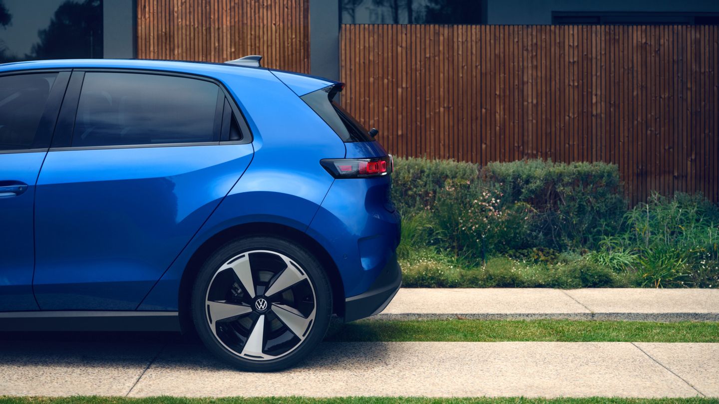 Bočný pohľad na zadnú časť modrého vozidla VW ID. Polo Style, ktoré stojí pred obytným domom so zelenou príjazdovou cestou.