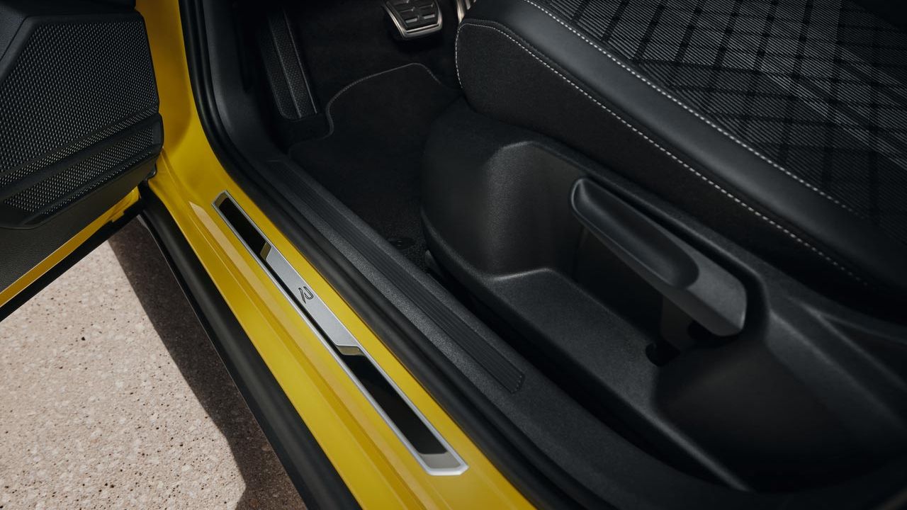 Pohľad na spodnú časť sedadla vodiča žltého VW T-Cross s otvorenými prednými dverami s prahovou lištou z brúsenej ušľachtilej ocele a logom R