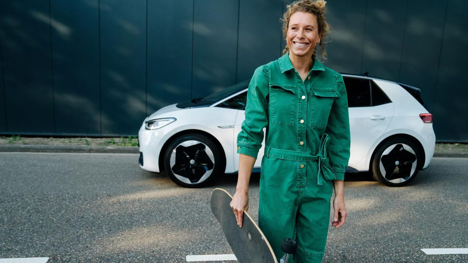 Žena so skateboardom pred elektrickým vozidlom