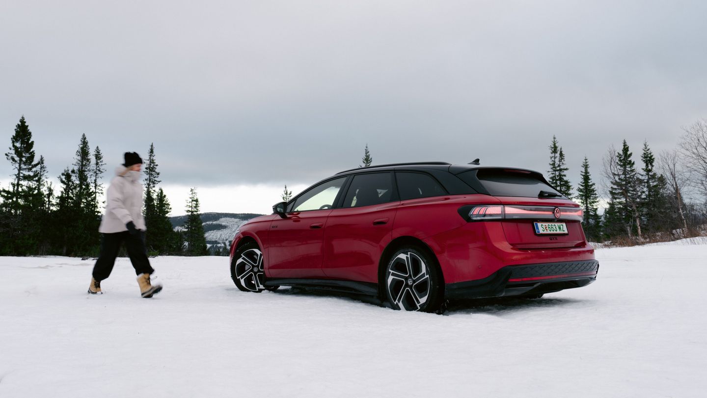 Žena kráča snehom smerom k červenému VW ID.7 Tourer GTX zaparkovanému v zimnej krajine.